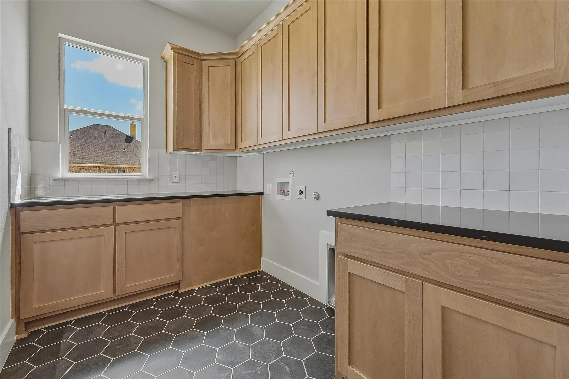 Hexagonal floor tiles, natural wood-finish cabinetry, dark countertops, white subway tile backsplash, and a large window