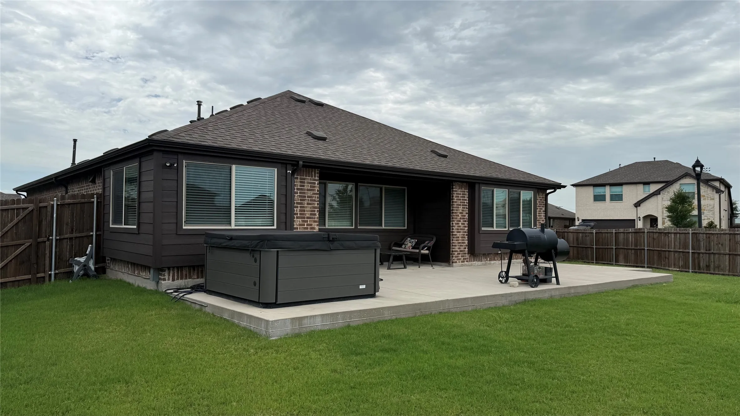 Spacious backyard with a large concrete patio, integrated hot tub, and a privacy fence