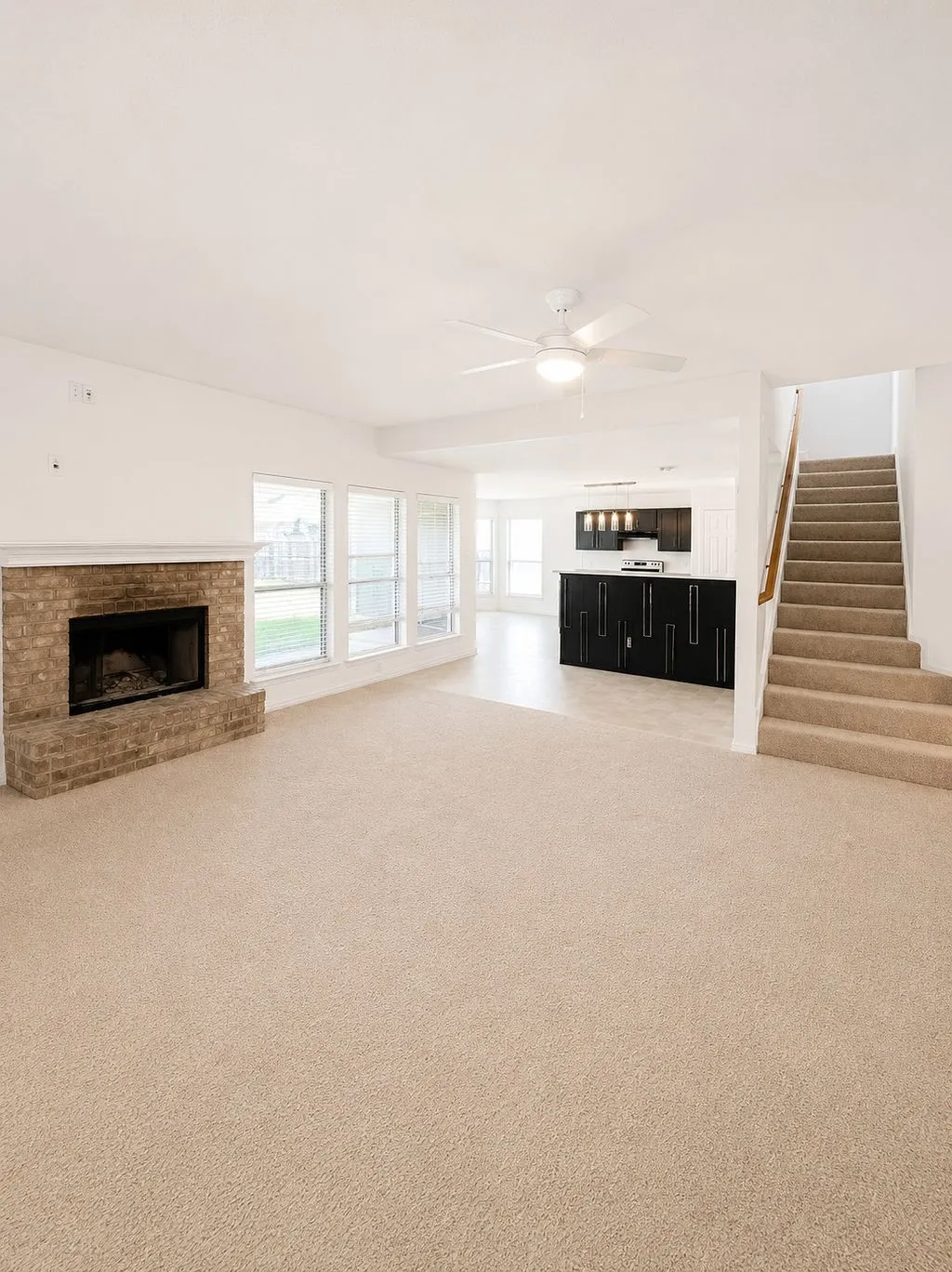 Spacious living area featuring neutral carpeting, a brick fireplace, and multiple windows
