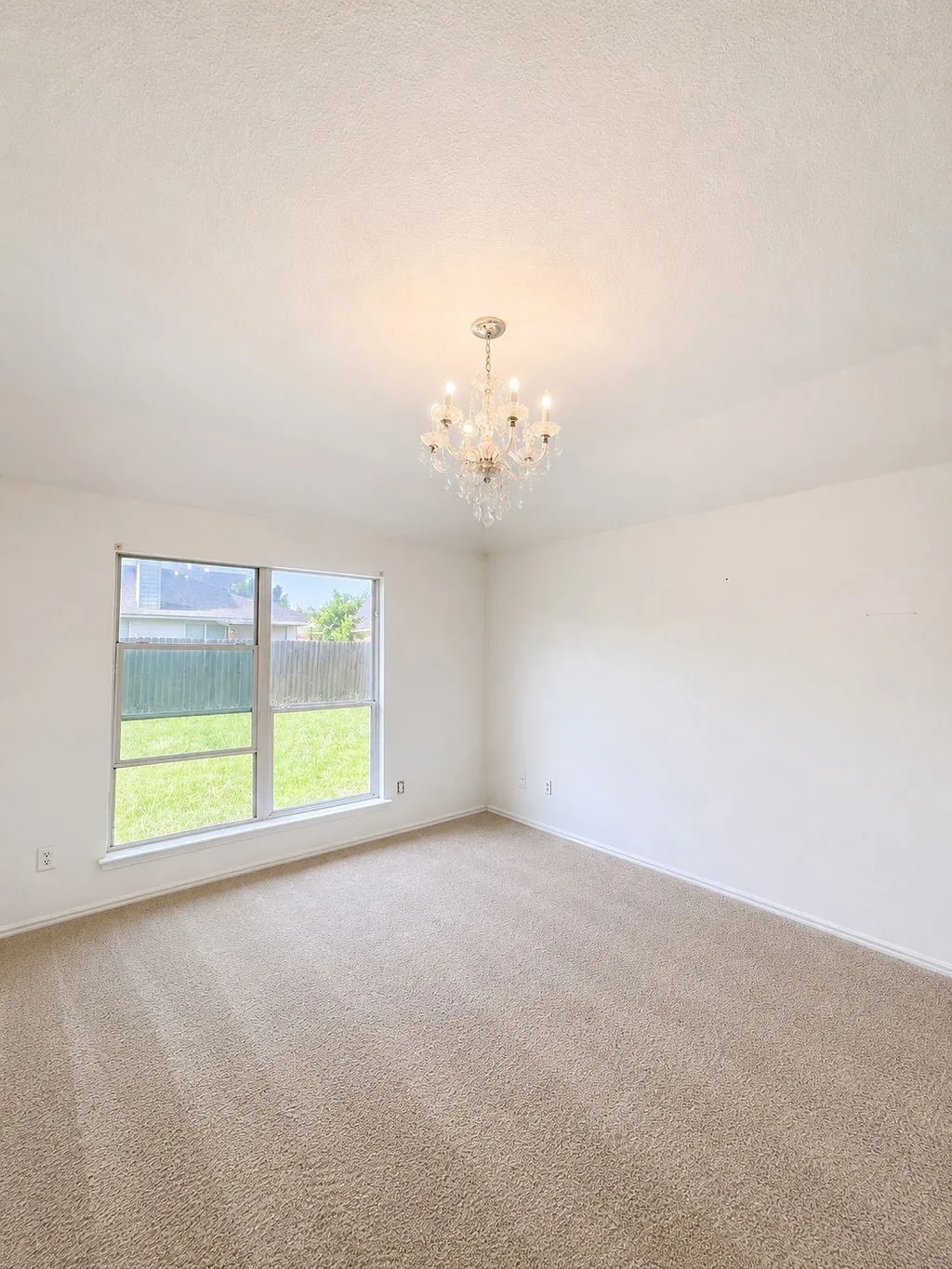 Room featuring a crystal chandelier, neutral-toned carpeting, and a large window providing natural light