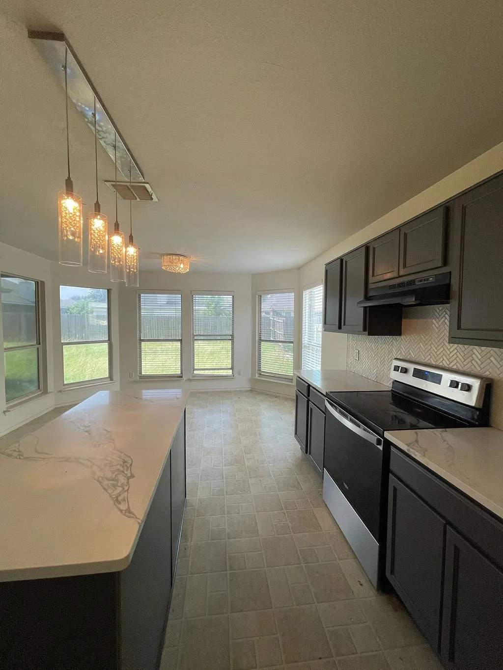 Kitchen featuring dark cabinetry, light-toned countertops with distinctive veining, a herringbone pattern tile backsplash, and stainless steel appliances