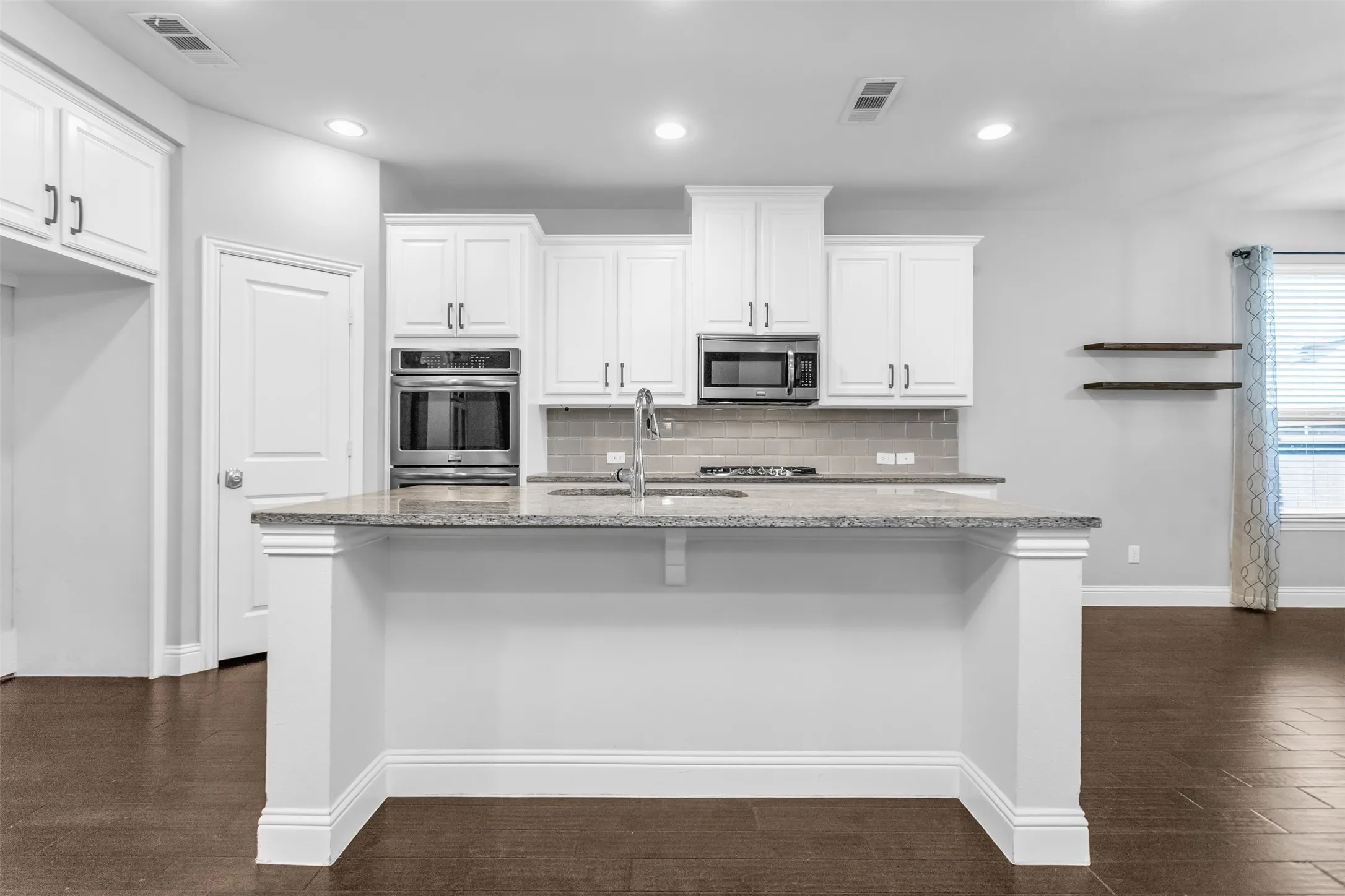Modern kitchen featuring a central island with a light-toned countertop, white cabinetry with dark hardware, stainless steel appliances, a subway tile backsplash, and dark wood-finish flooring
