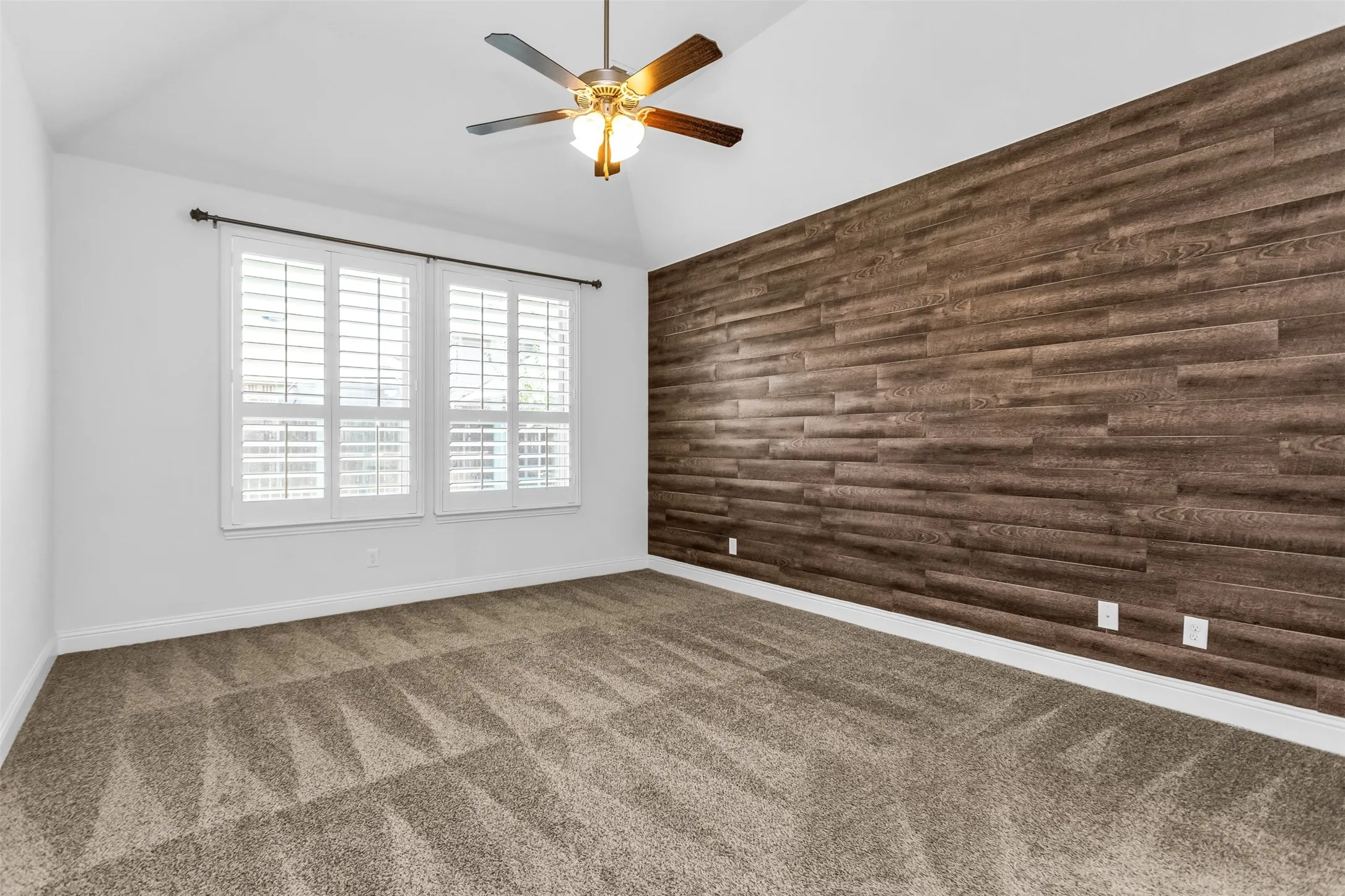 Spacious room featuring a vaulted ceiling and a wood-paneled accent wall