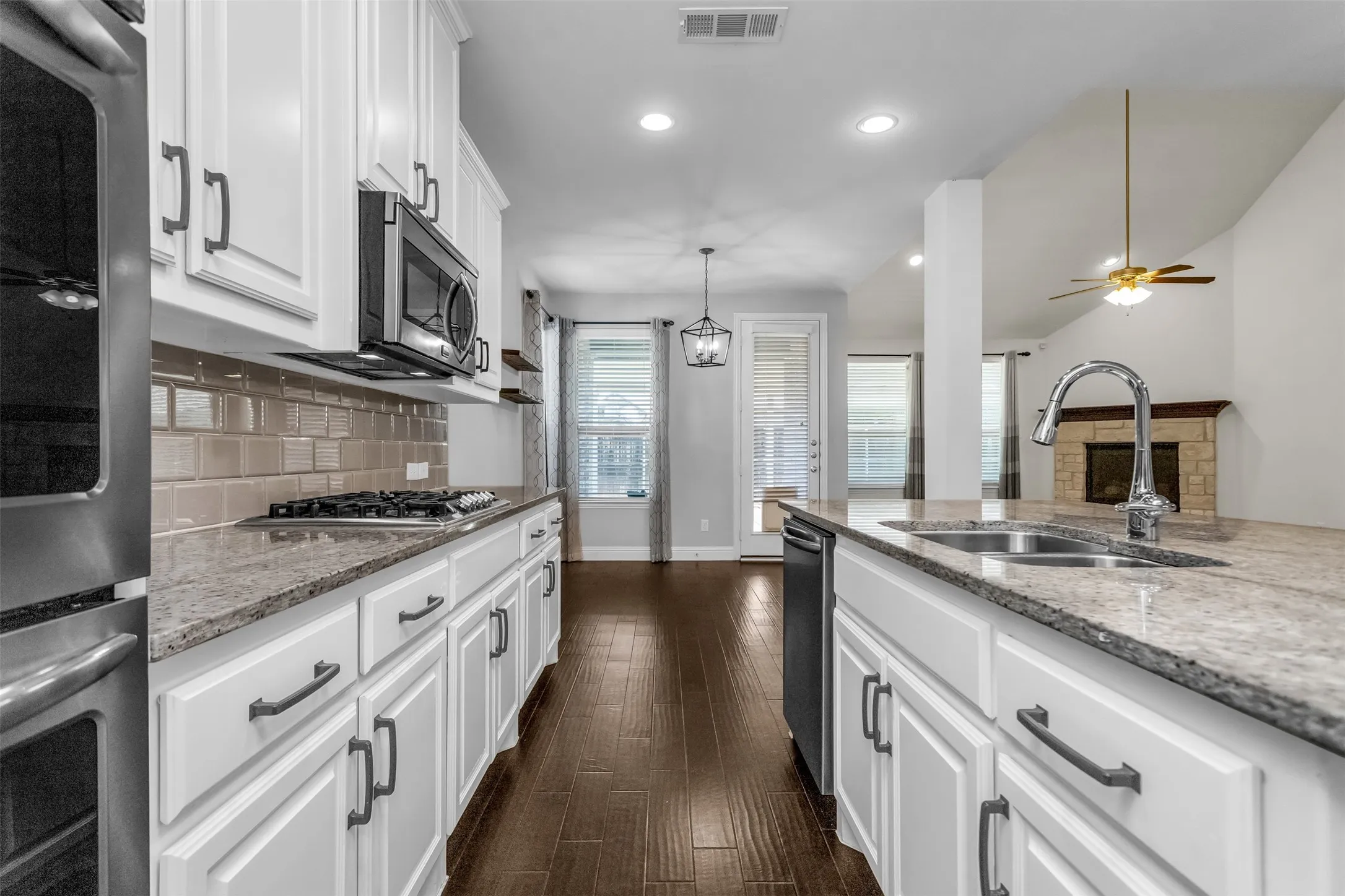 Kitchen showcasing white cabinetry with dark hardware, granite countertops, subway tile backsplash, and stainless steel appliances including an oven, microwave, and dishwasher