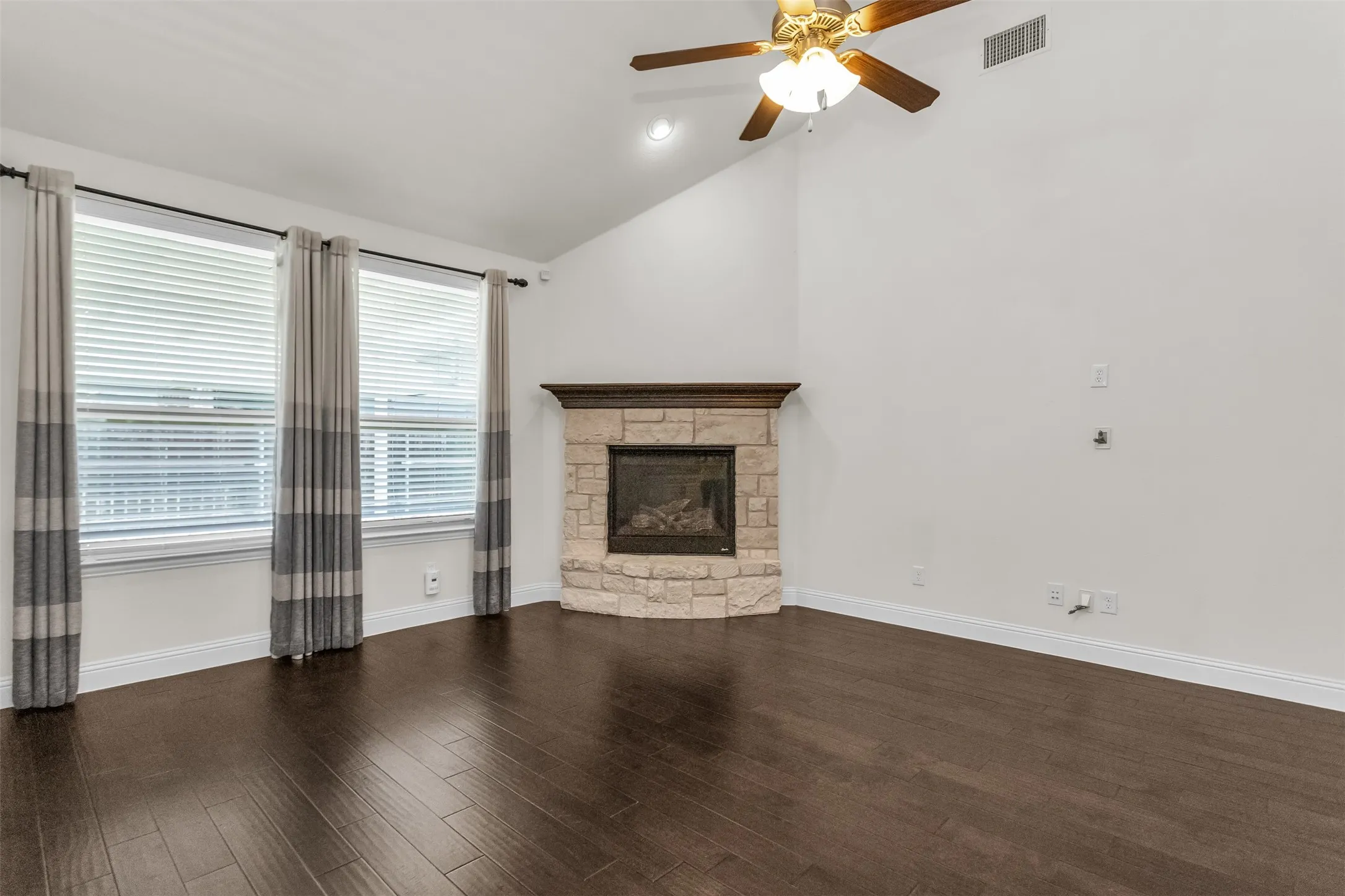 Living area featuring a corner stone fireplace with a wood mantle, vaulted ceiling with a ceiling fan, and wood-finish flooring