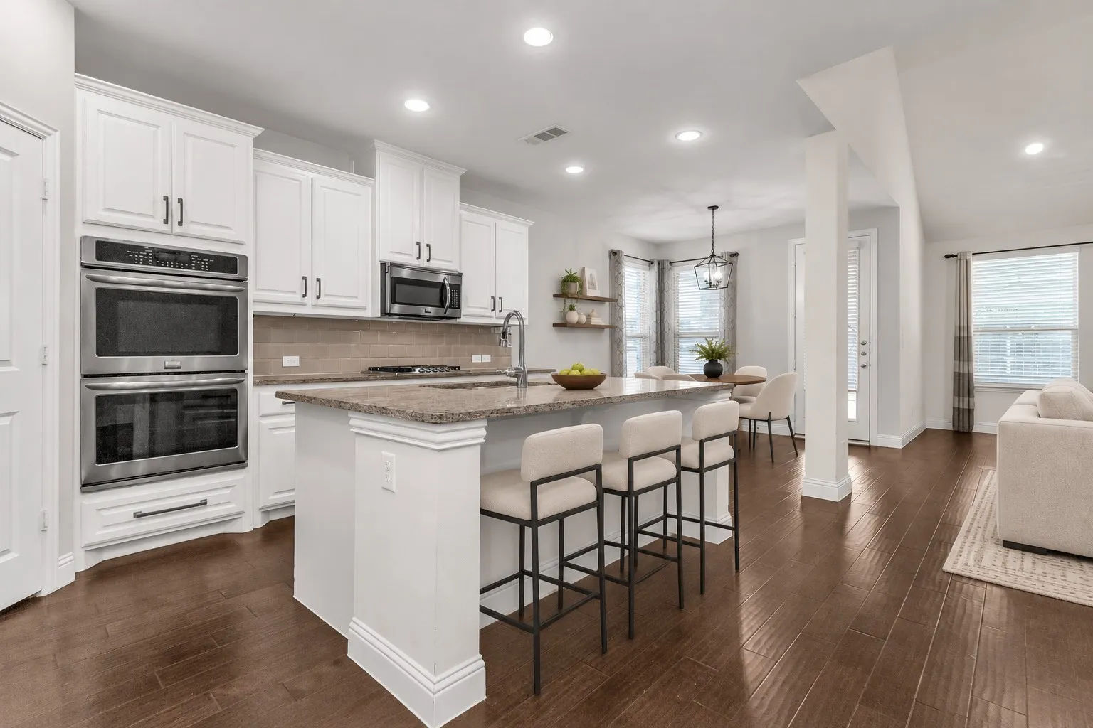Spacious kitchen featuring white cabinetry, stainless steel double ovens, a central island with countertop seating, and wood-finish flooring
