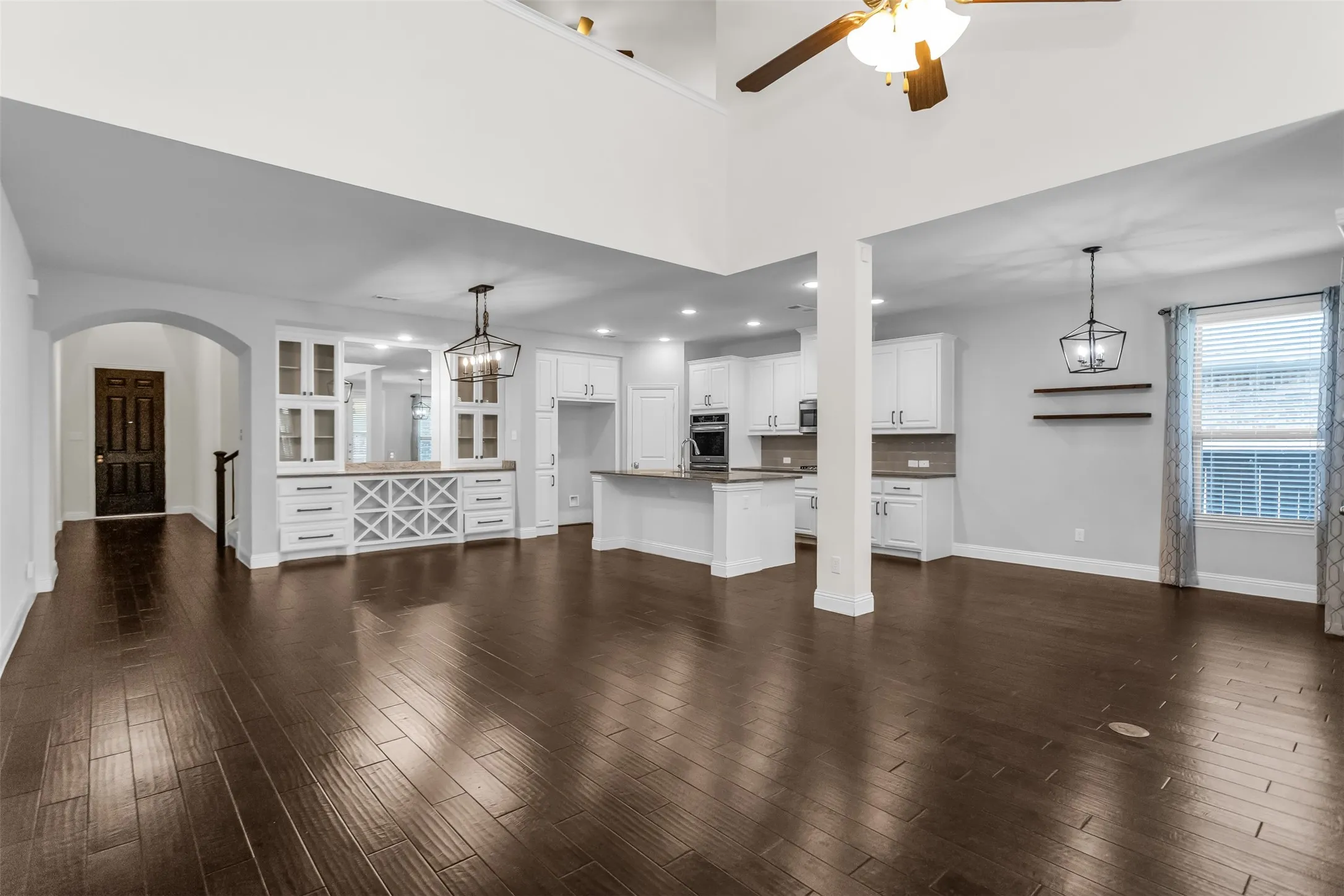 Expansive open-concept living space featuring high ceilings, dark wood-finish flooring, and a built-in cabinetry unit with glass display doors