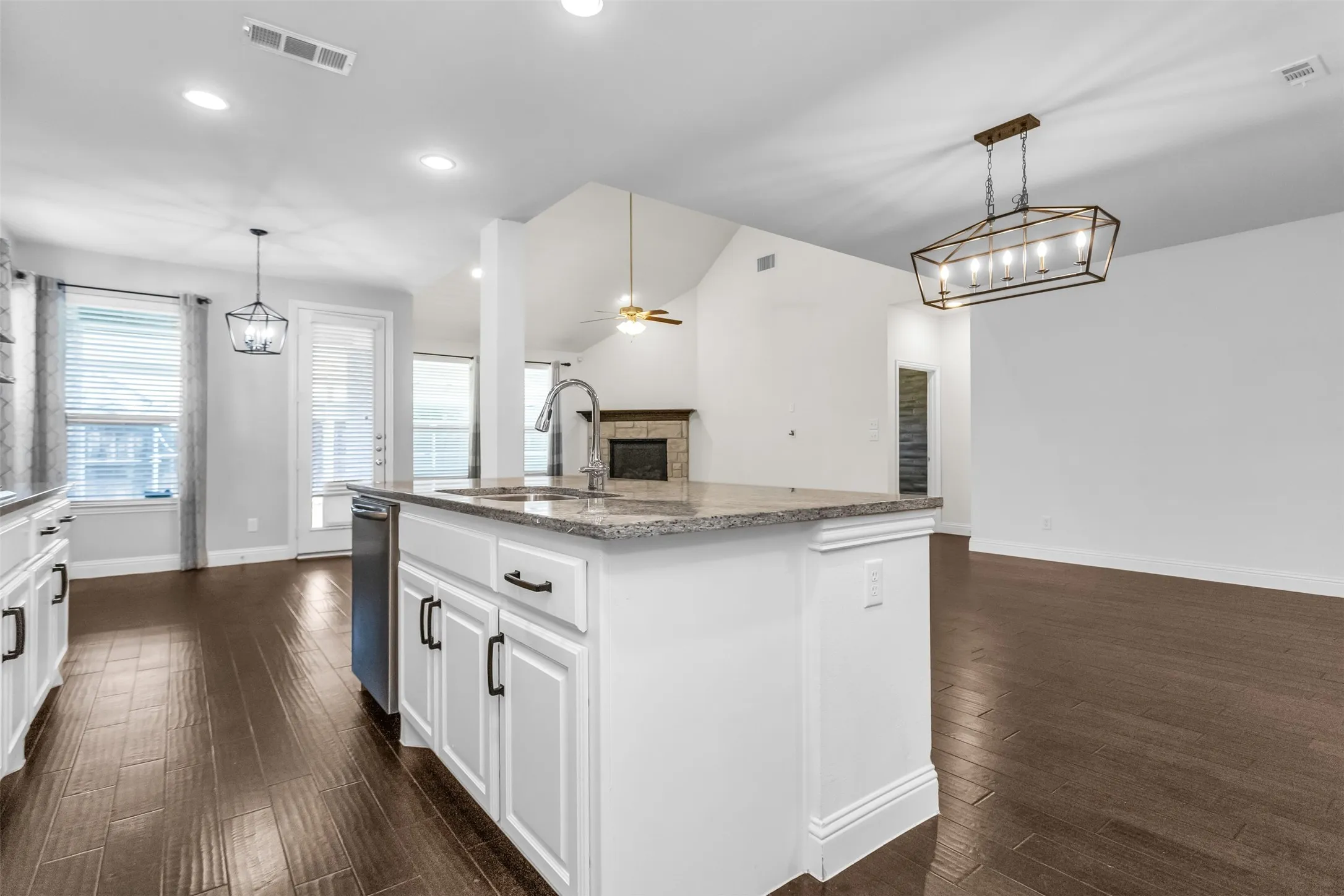 Kitchen island featuring a granite countertop, undermount sink with gooseneck faucet, white cabinetry, and a dishwasher