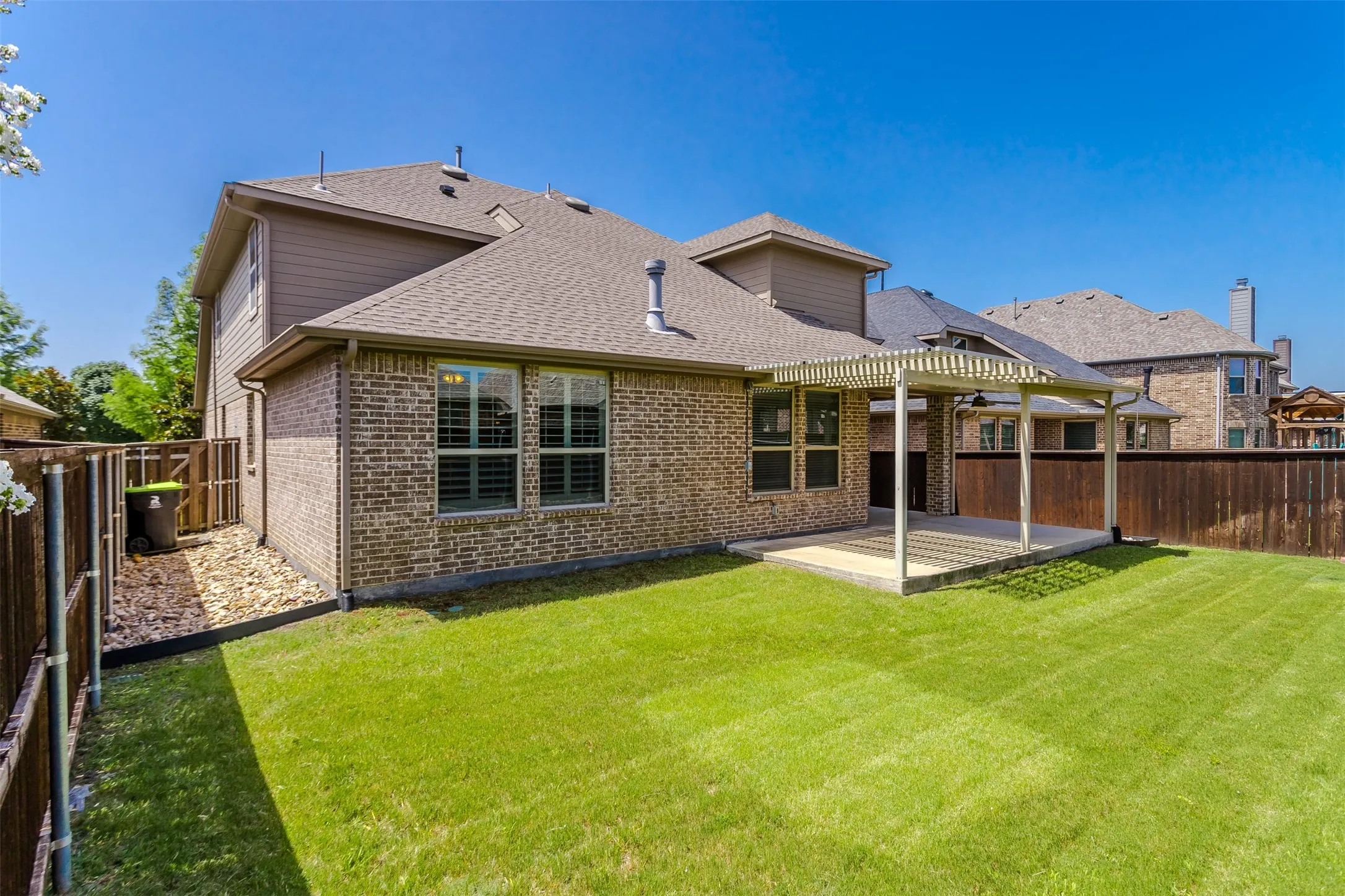Expansive backyard featuring a manicured lawn, a large covered patio with a ceiling fan, and a perimeter wood fence