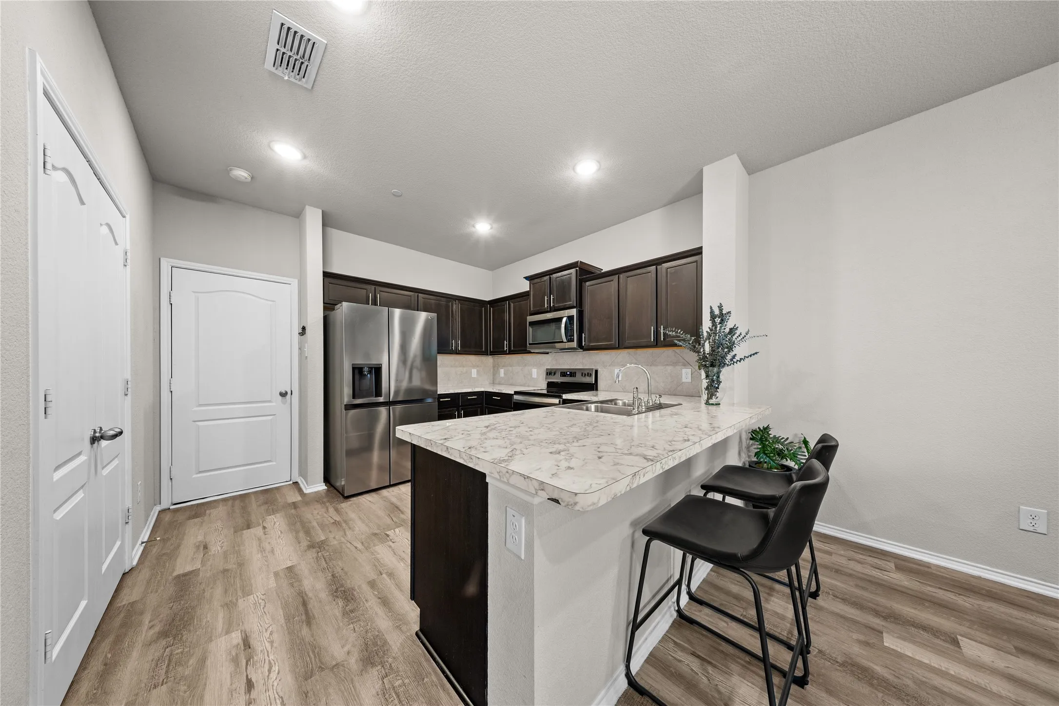 Modern kitchen featuring stainless steel appliances, white quartz waterfall island countertop, dark cabinetry with contrasting white upper cabinetry, recessed ceiling lighting, and wood-finish flooring throughout