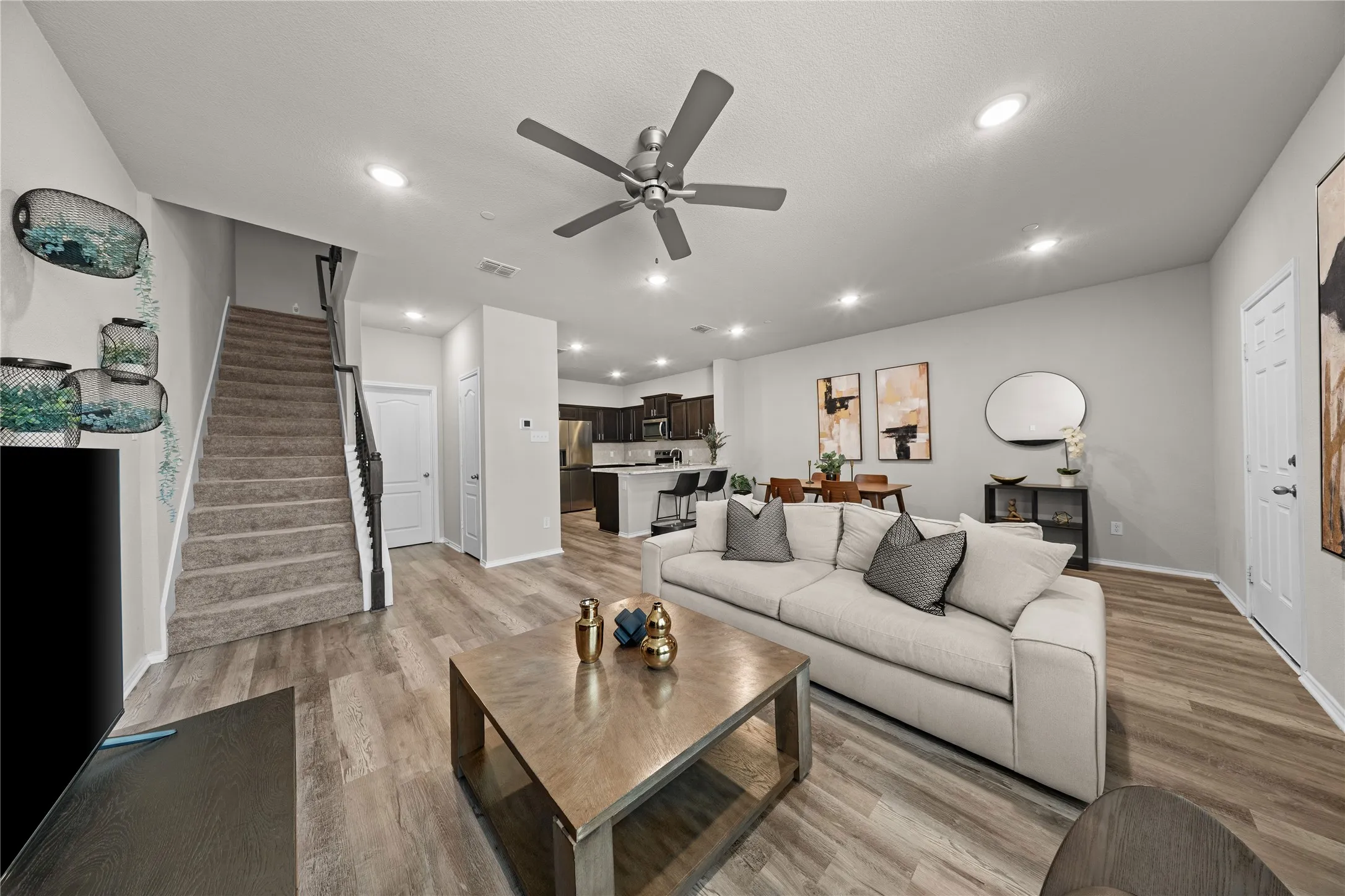 Open-concept living space featuring a light gray upholstered sectional, wood-finish flooring throughout, and a wood coffee table
