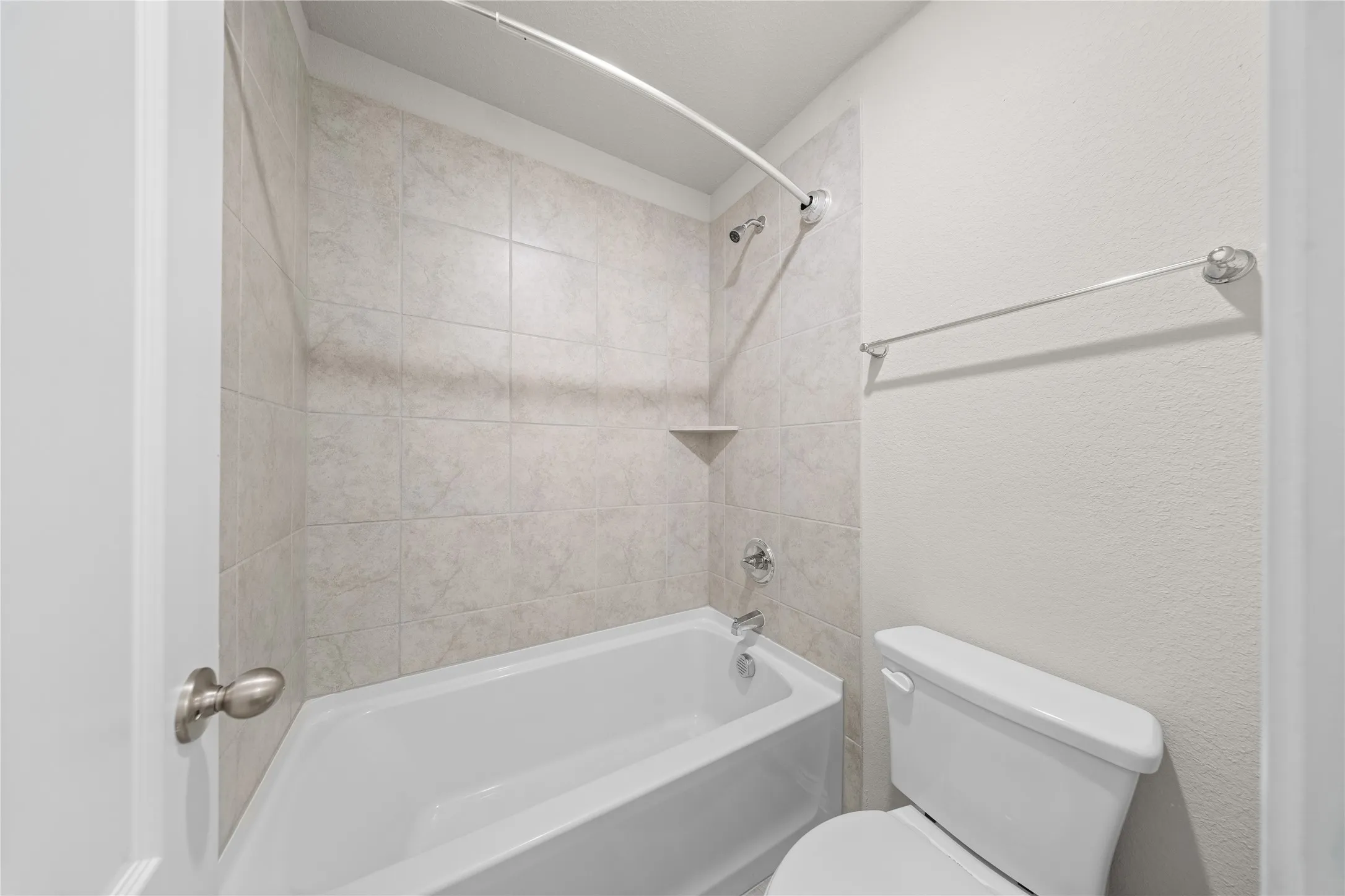 Bathroom featuring a tile-surrounded bathtub, integrated shower, corner shelf, and commode
