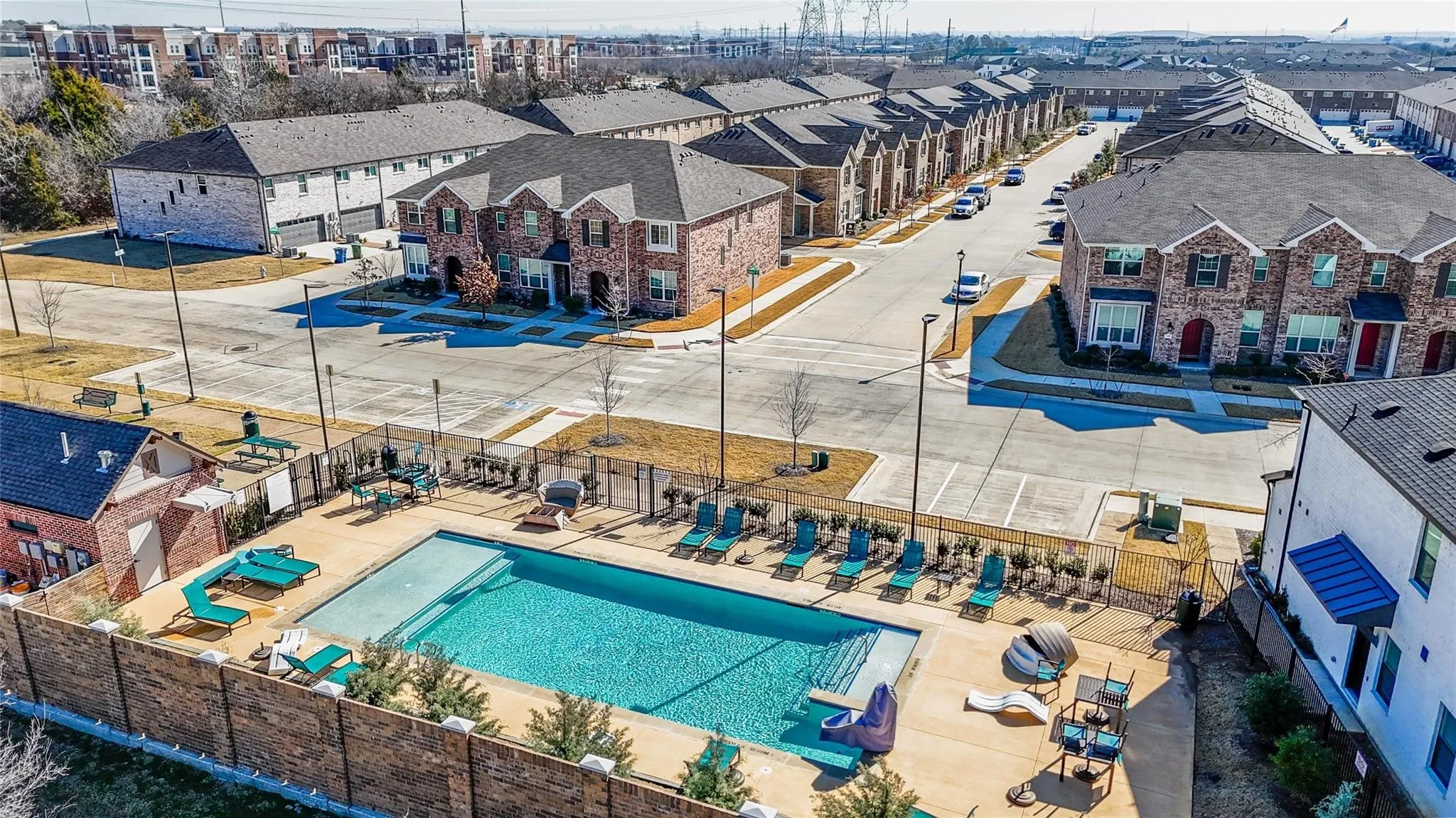 Community swimming pool with surrounding concrete patio, enclosed by a wood-paneled fence with brick accents