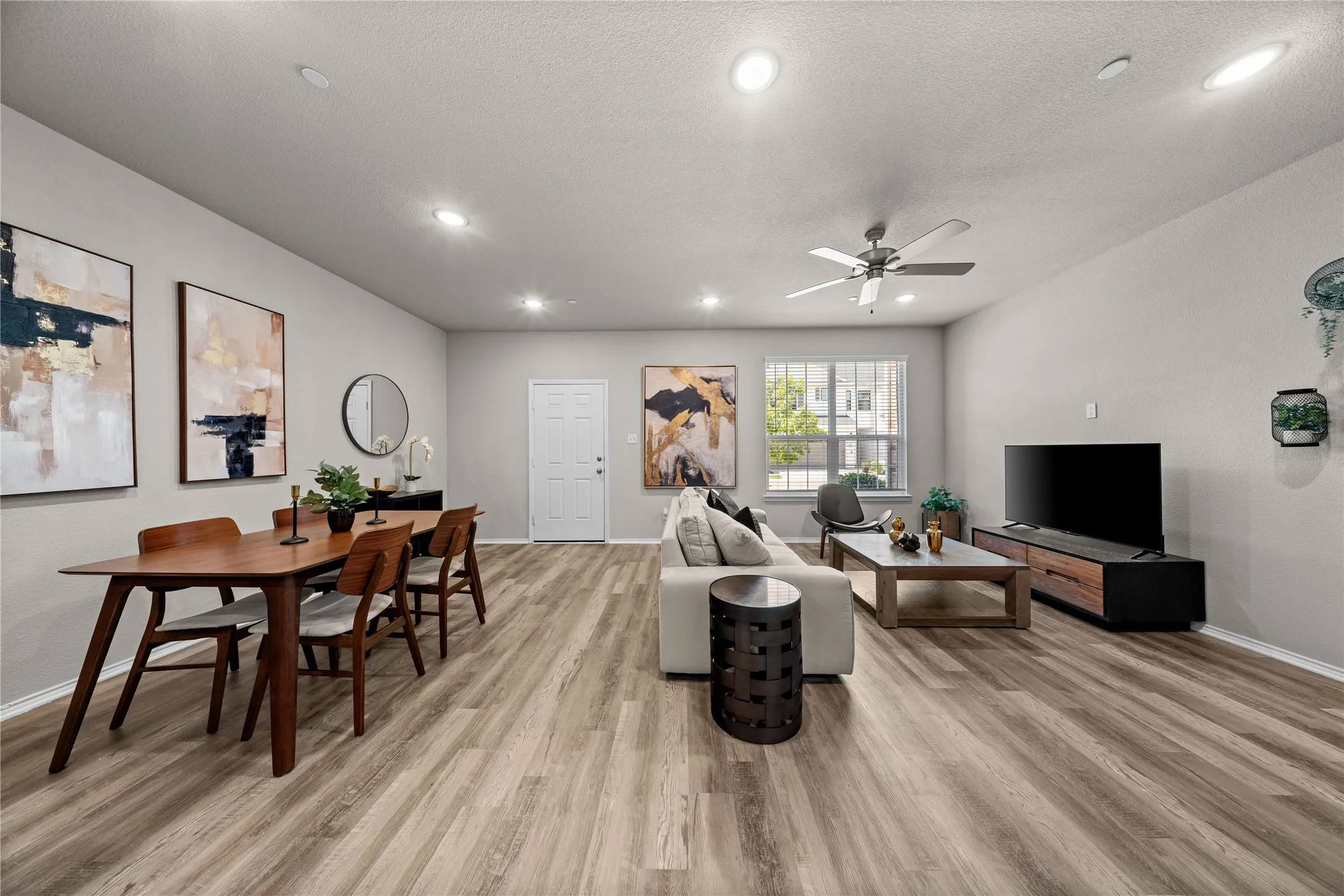 Open-concept living space featuring wood-finish flooring throughout, recessed and ceiling fan lighting, and seamless integration of dining and entertainment areas