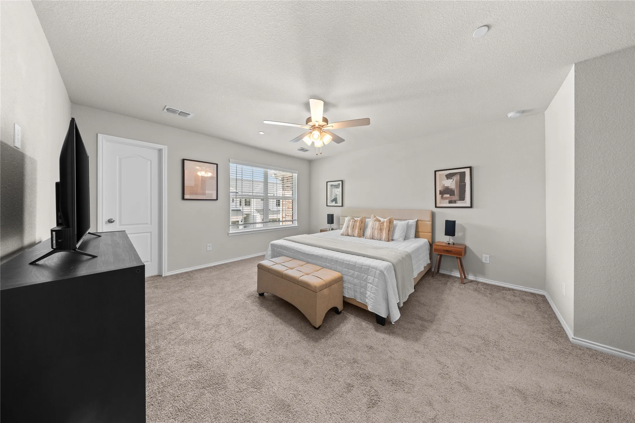 Spacious room featuring neutral carpeting, a ceiling fan with integrated lighting, and a large window providing ample natural light