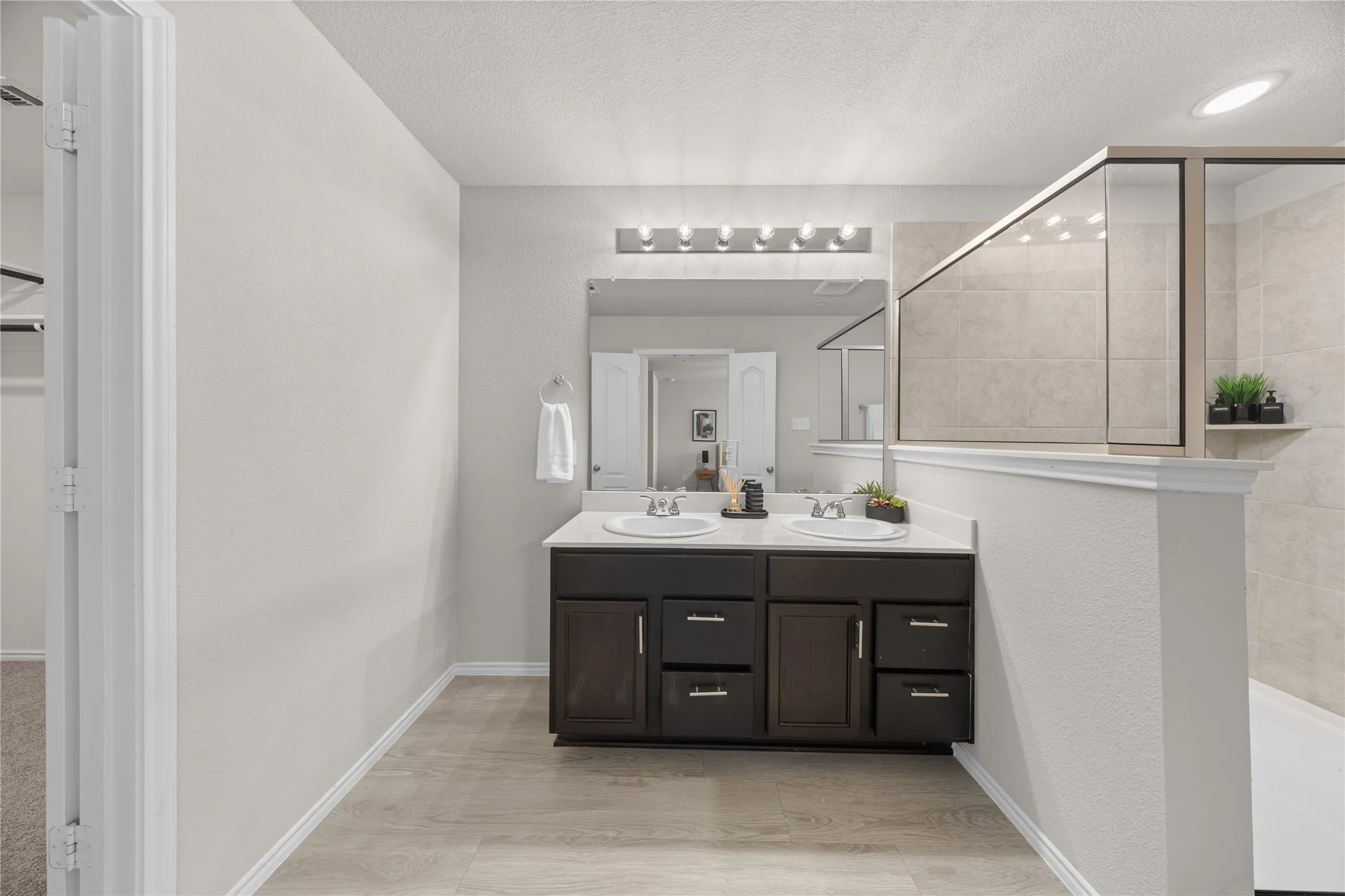 Bathroom featuring a dual-sink vanity with dark wood-finish cabinetry, a large frameless mirror, and overhead strip lighting