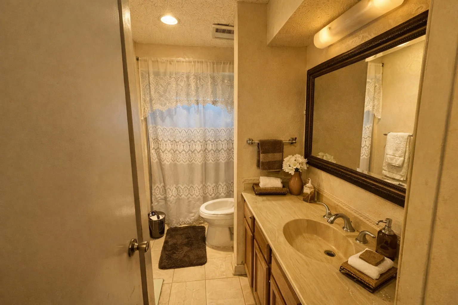 Bathroom featuring a spacious vanity with an integrated sink, framed mirror, warm-toned cabinetry, tiled flooring, and a shower/tub combination with a window