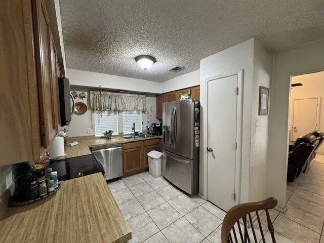 Kitchen featuring wood cabinetry, stainless steel appliances, a double basin sink, and tile flooring