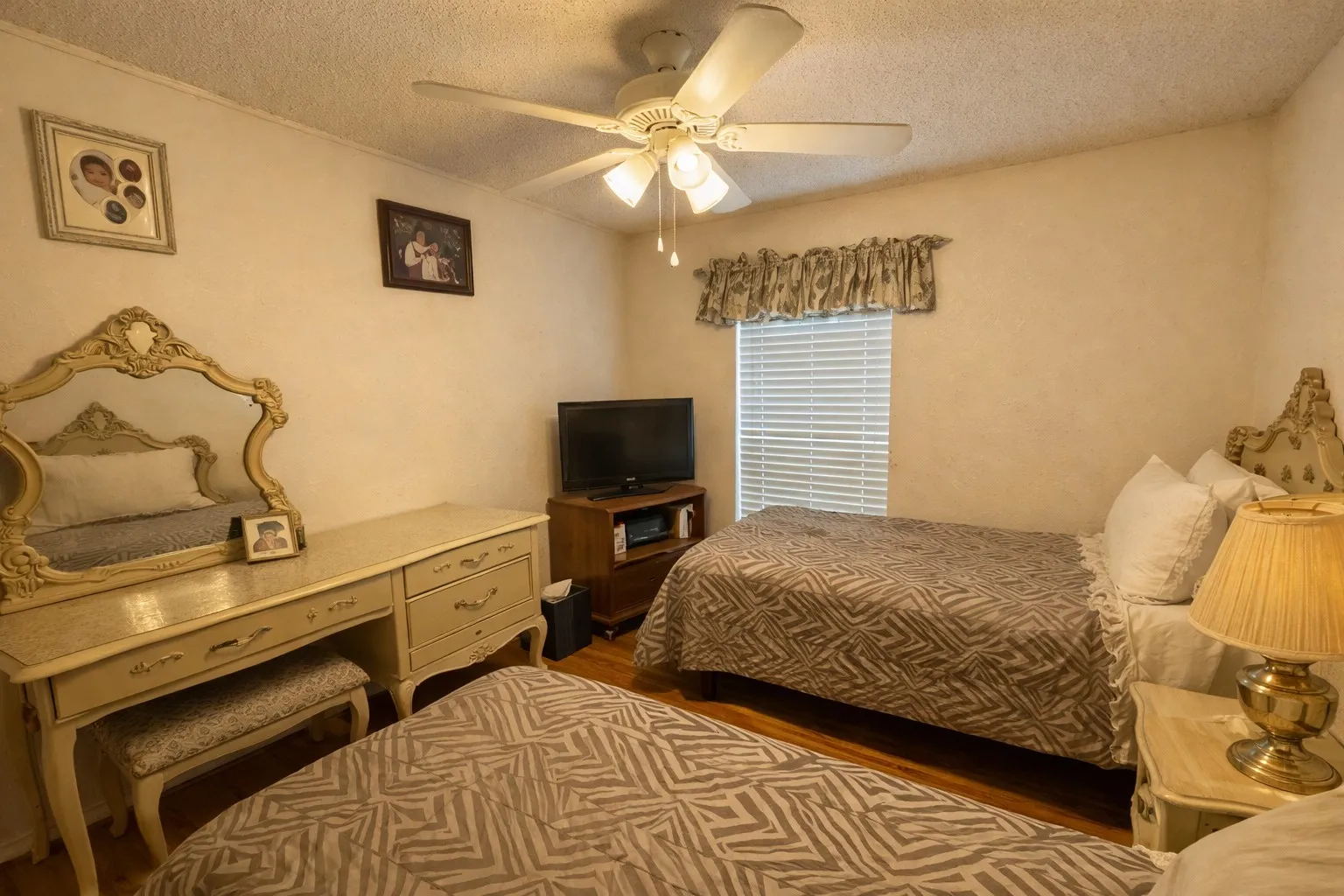 Room featuring a ceiling fan with light fixture, wood-finish flooring, and a window with horizontal blinds and a valance