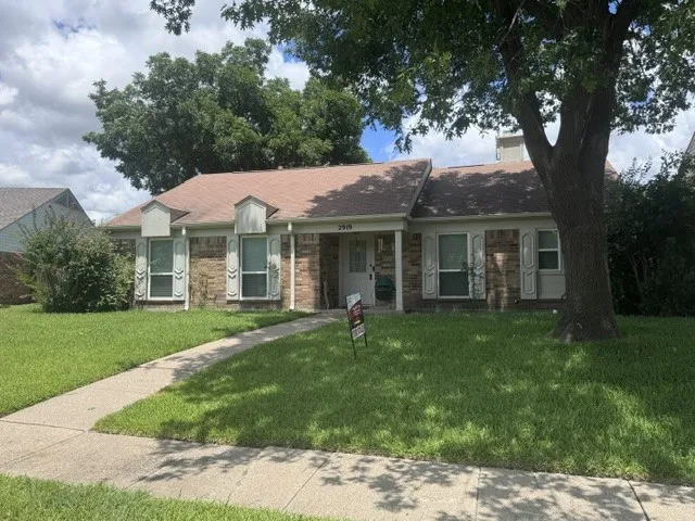 Brick-front exterior featuring a light-colored roof, decorative window shutters, and a mature tree