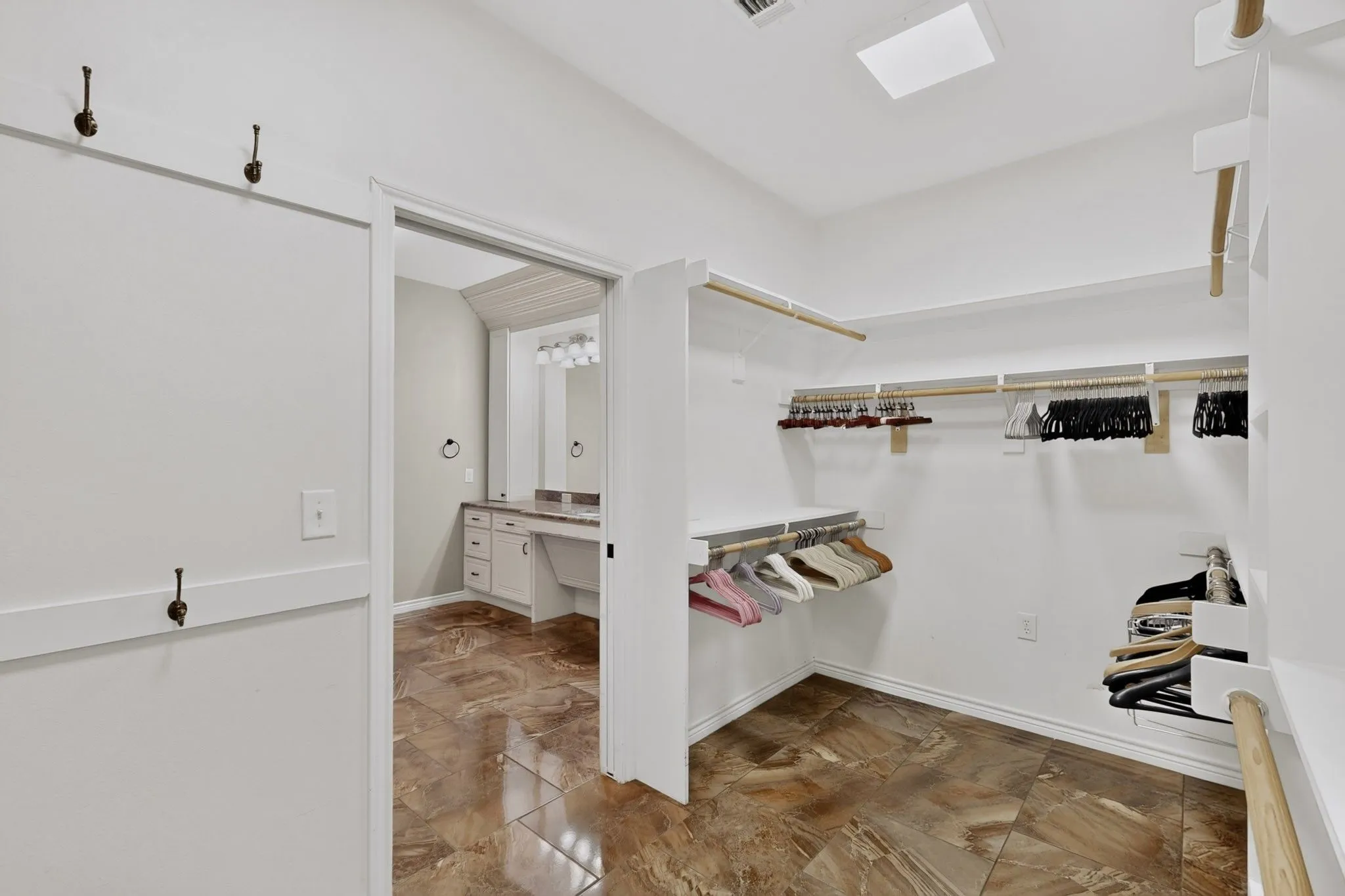 Spacious walk-in closet featuring extensive built-in shelving, multiple hanging rods, durable tile flooring, and overhead lighting