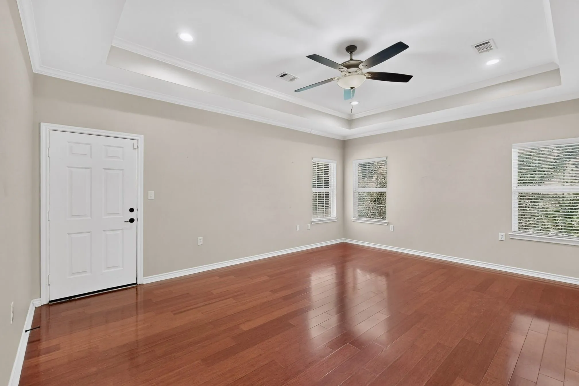 Spacious room featuring rich wood-finish flooring, a tray ceiling with recessed lighting, and a ceiling fan