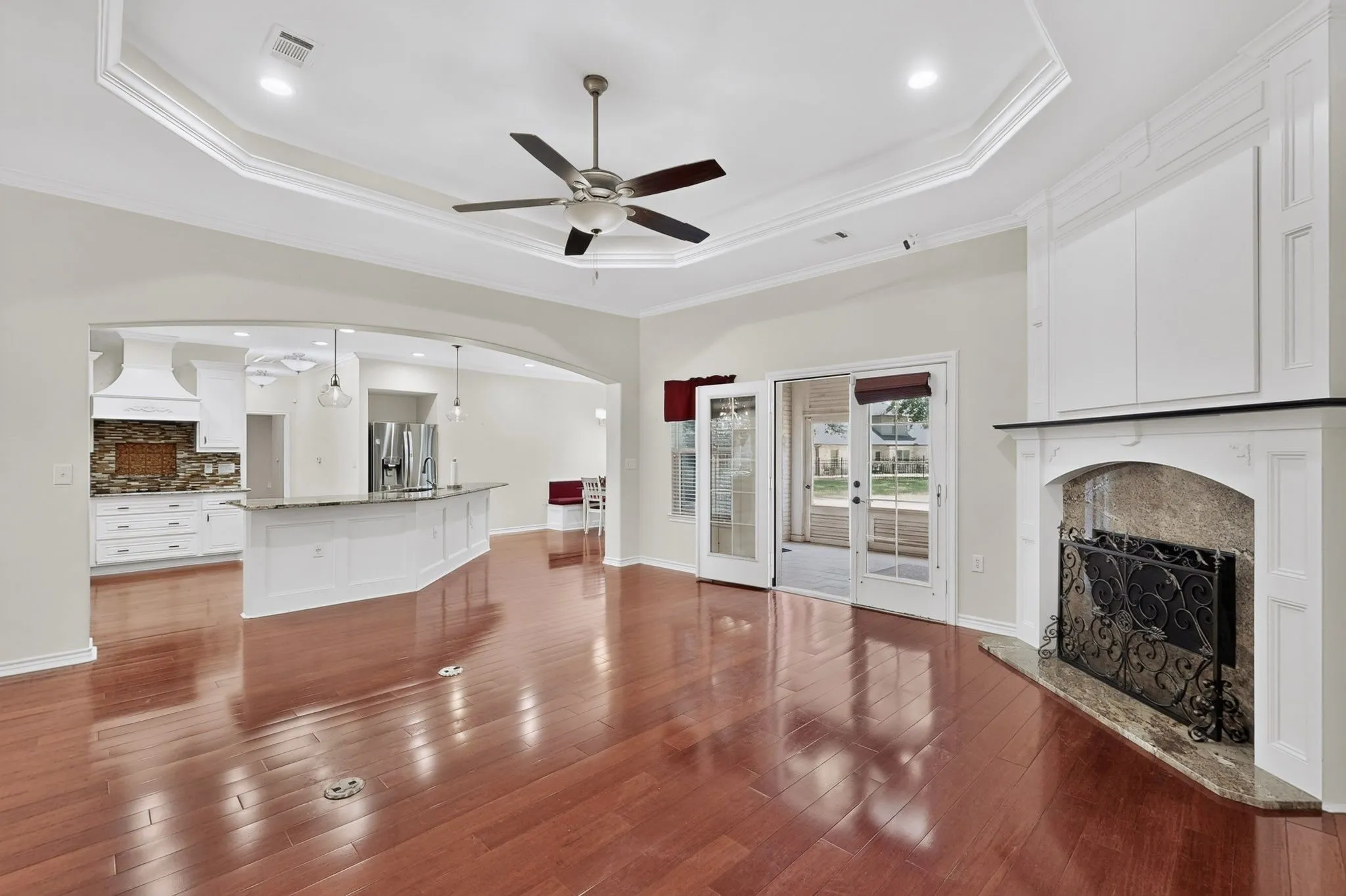 Spacious room featuring wood-finish flooring, a tray ceiling with a fan, and a fireplace with a decorative mantel and hearth