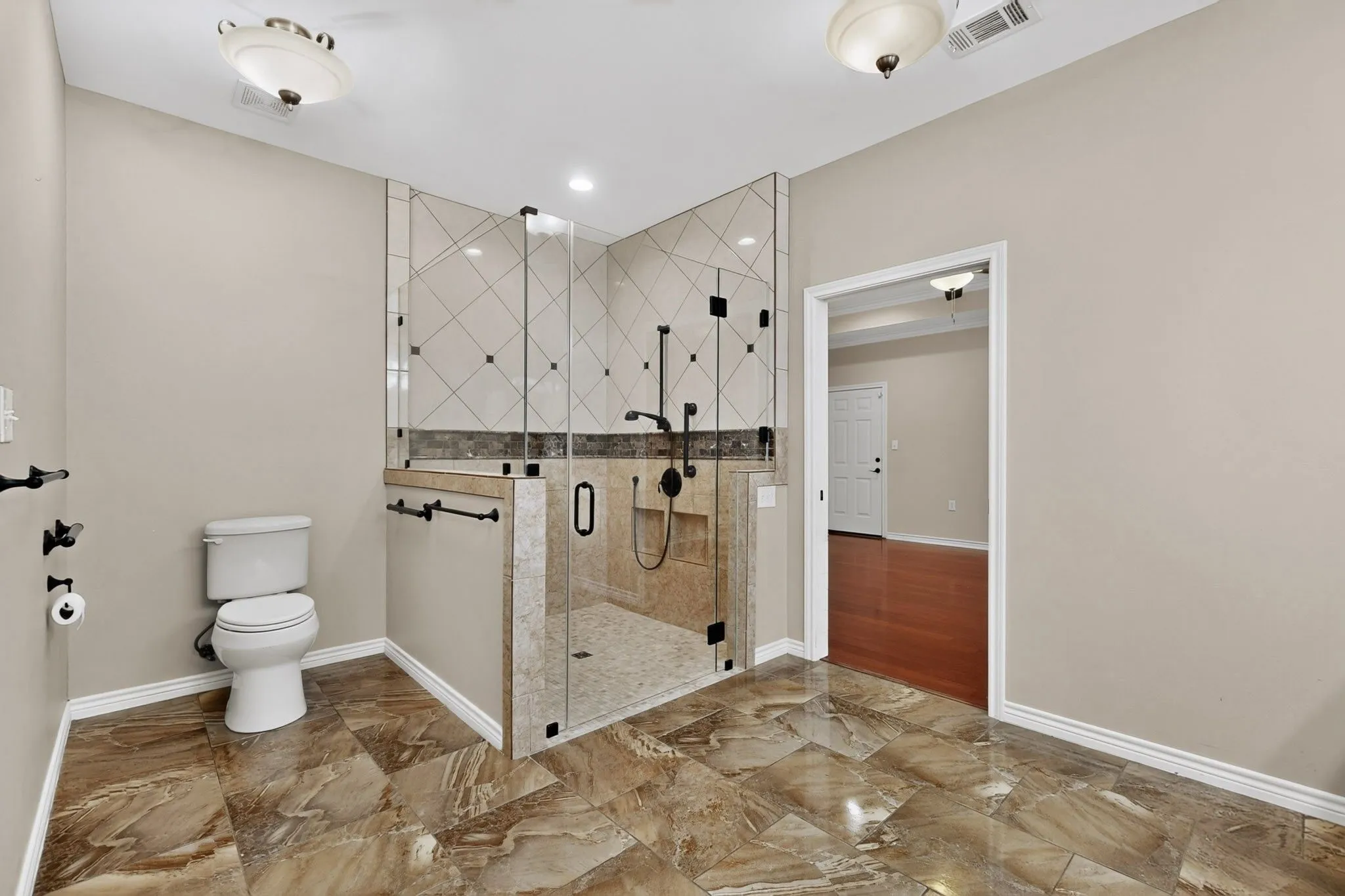 Spacious bathroom featuring large format floor tiling, a clear glass enclosed shower with a built-in bench, geometric tile shower surround, and matte black fixtures
