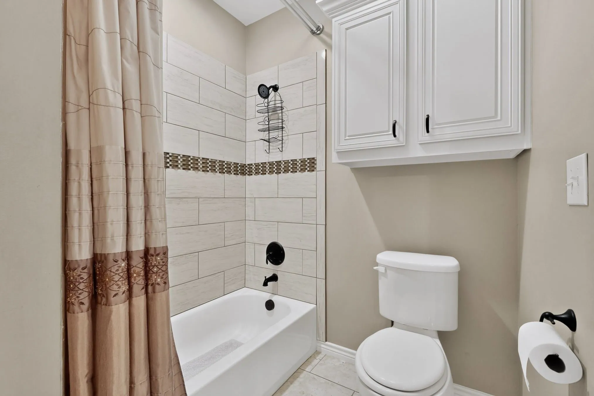 Bathtub and shower combination featuring subway tile with a decorative accent band, complemented by a black-finish showerhead and faucet