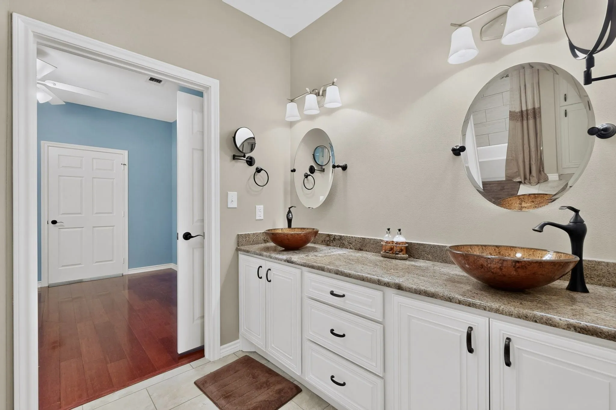 Double vanity featuring vessel sinks, stone-finish countertops, and white cabinetry with dark hardware