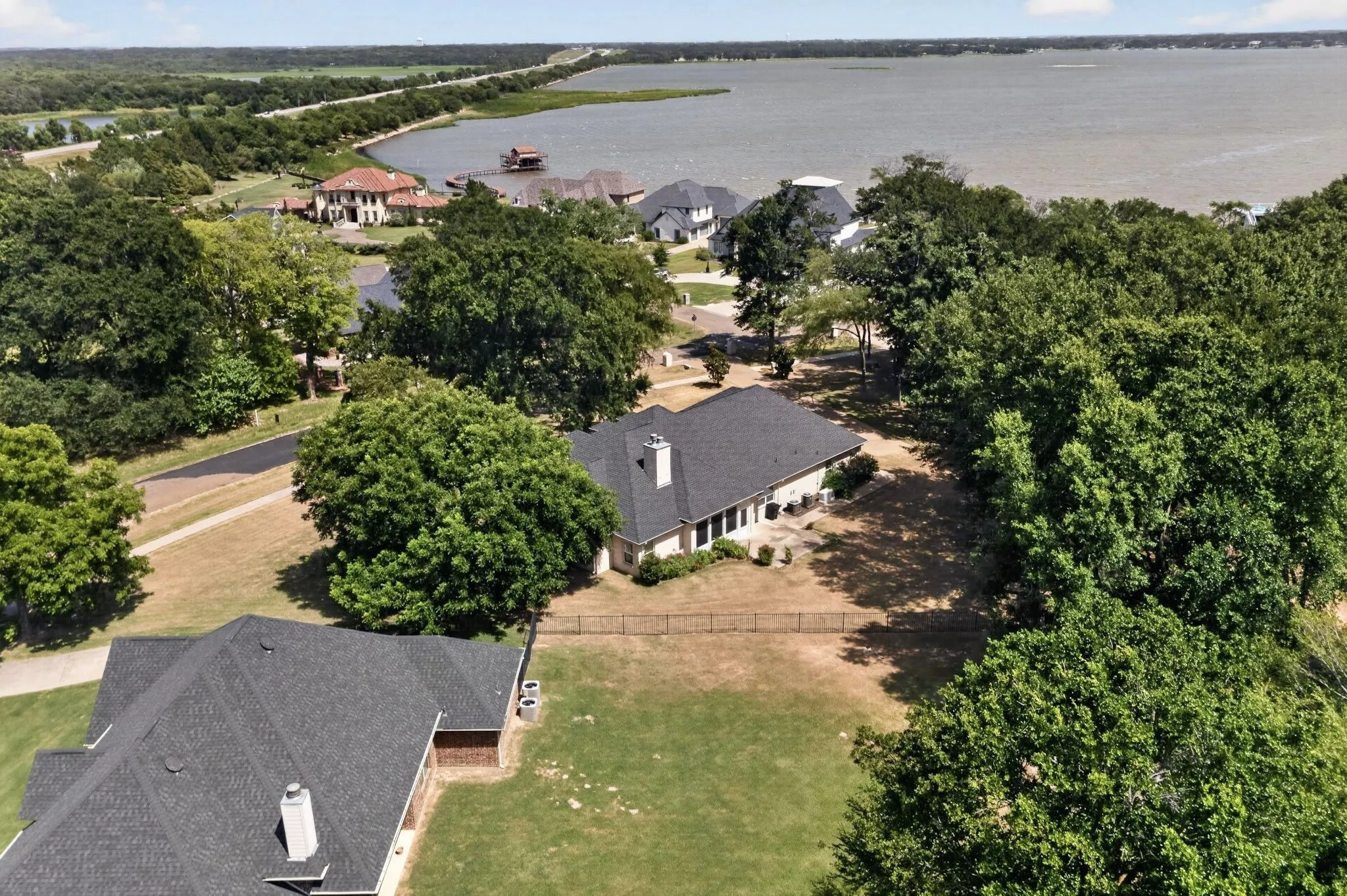 Waterfront property featuring a dark shingle roof, established landscaping, and a partial fenced yard