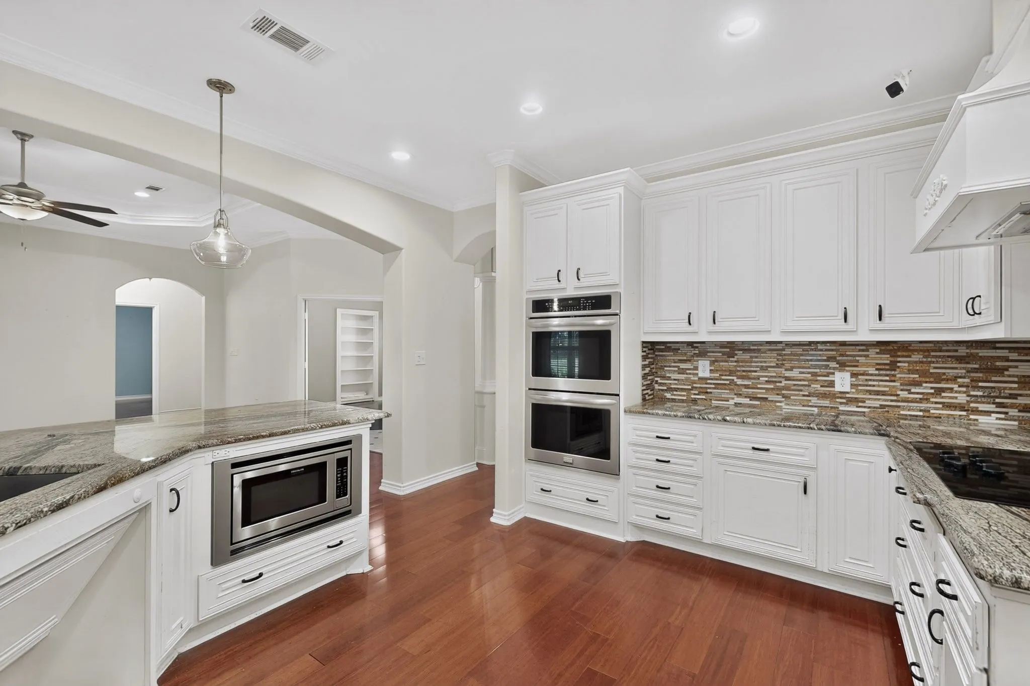 Kitchen featuring hardwood flooring, white cabinetry, granite countertops, stainless steel appliances, and a mosaic tile backsplash