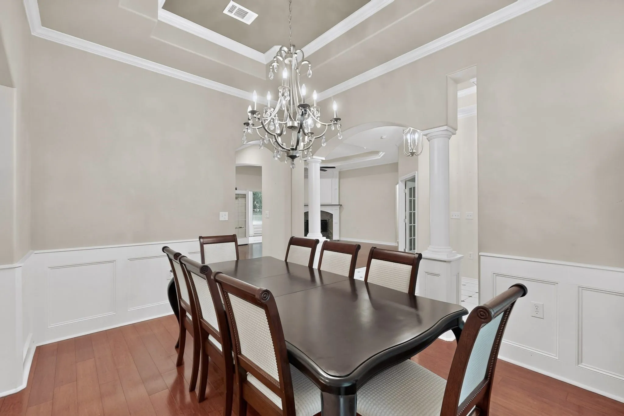Dining area featuring wood-finish flooring, wainscoting, and a multi-tiered tray ceiling with a crystal chandelier