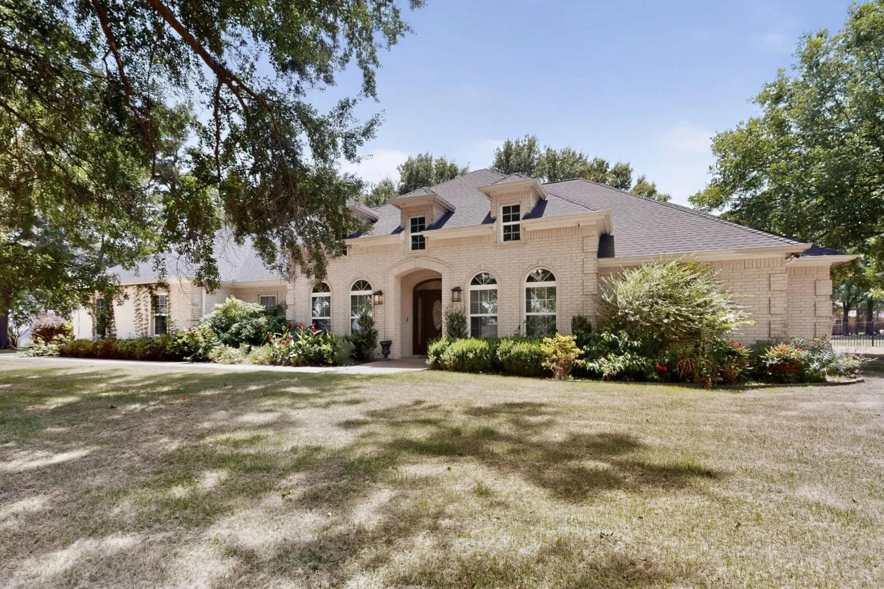 Light-colored brick exterior featuring an arched entry, dormer windows, and a dark shingle roof