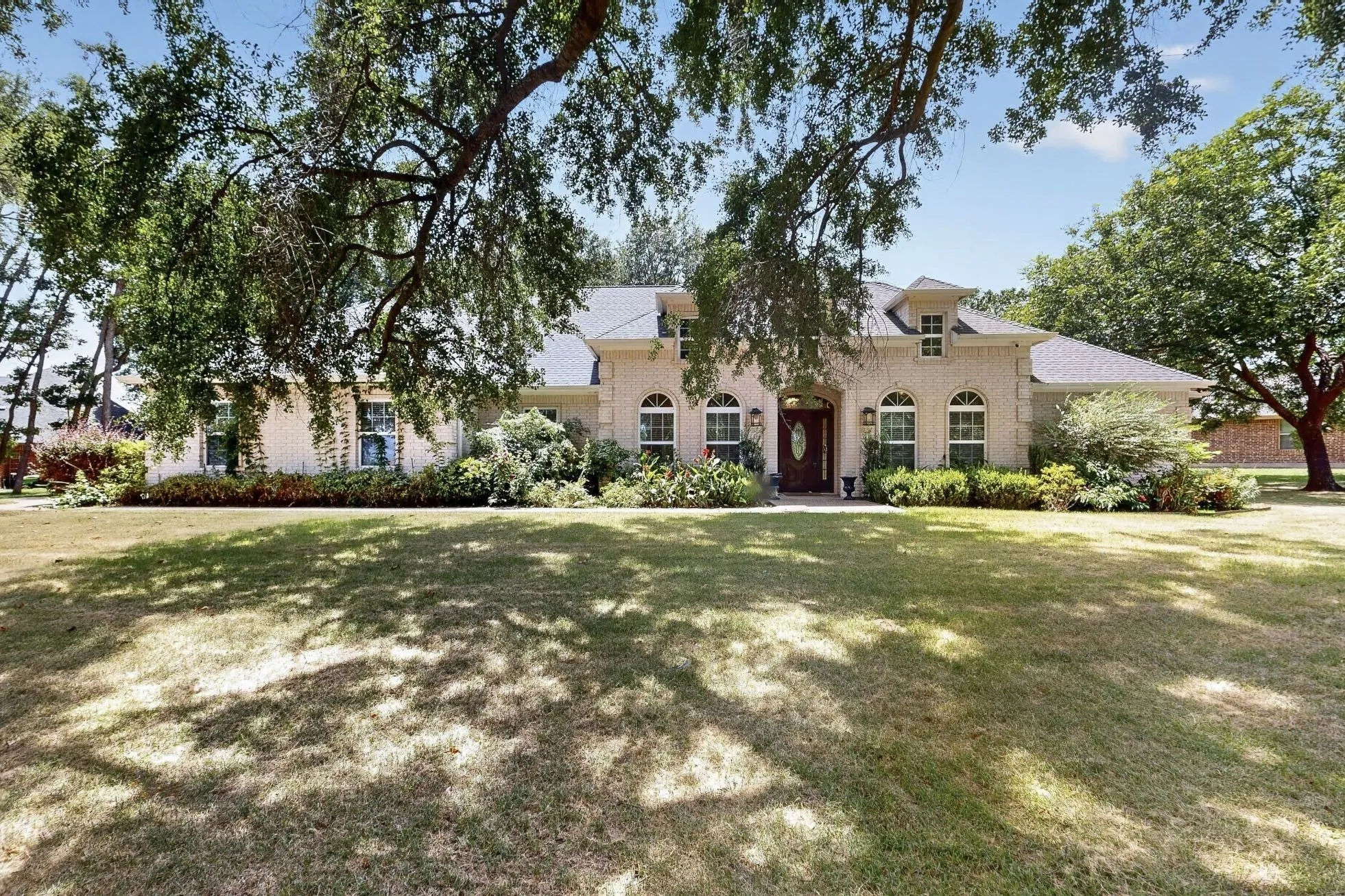 Traditional-style residence featuring a light-colored brick exterior, a dark shingle roof, and multiple dormer windows
