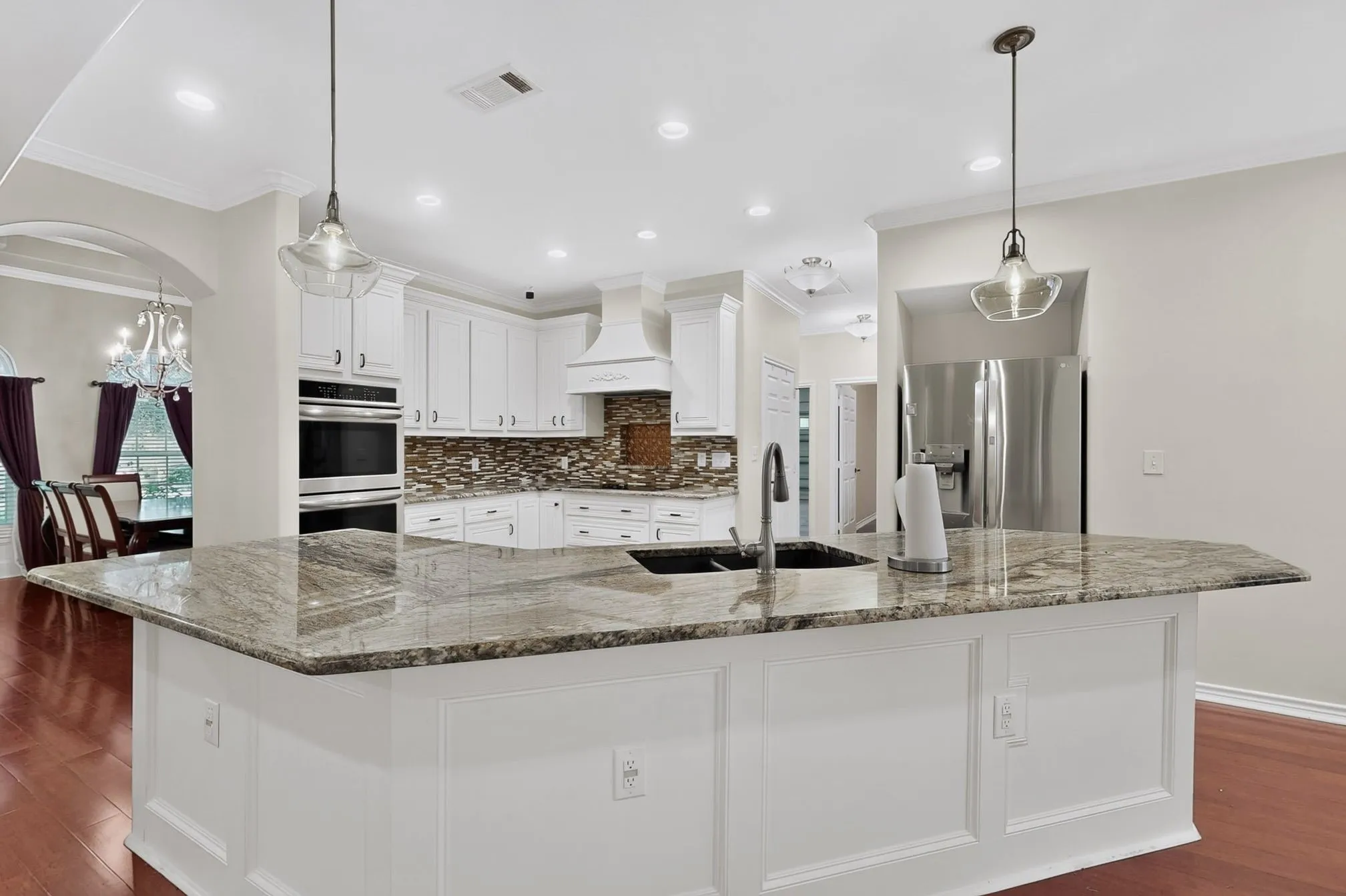 Kitchen featuring a large island with an undermount sink and a stone-finish countertop, white cabinetry with dark hardware, integrated stainless steel appliances, and wood-finish flooring