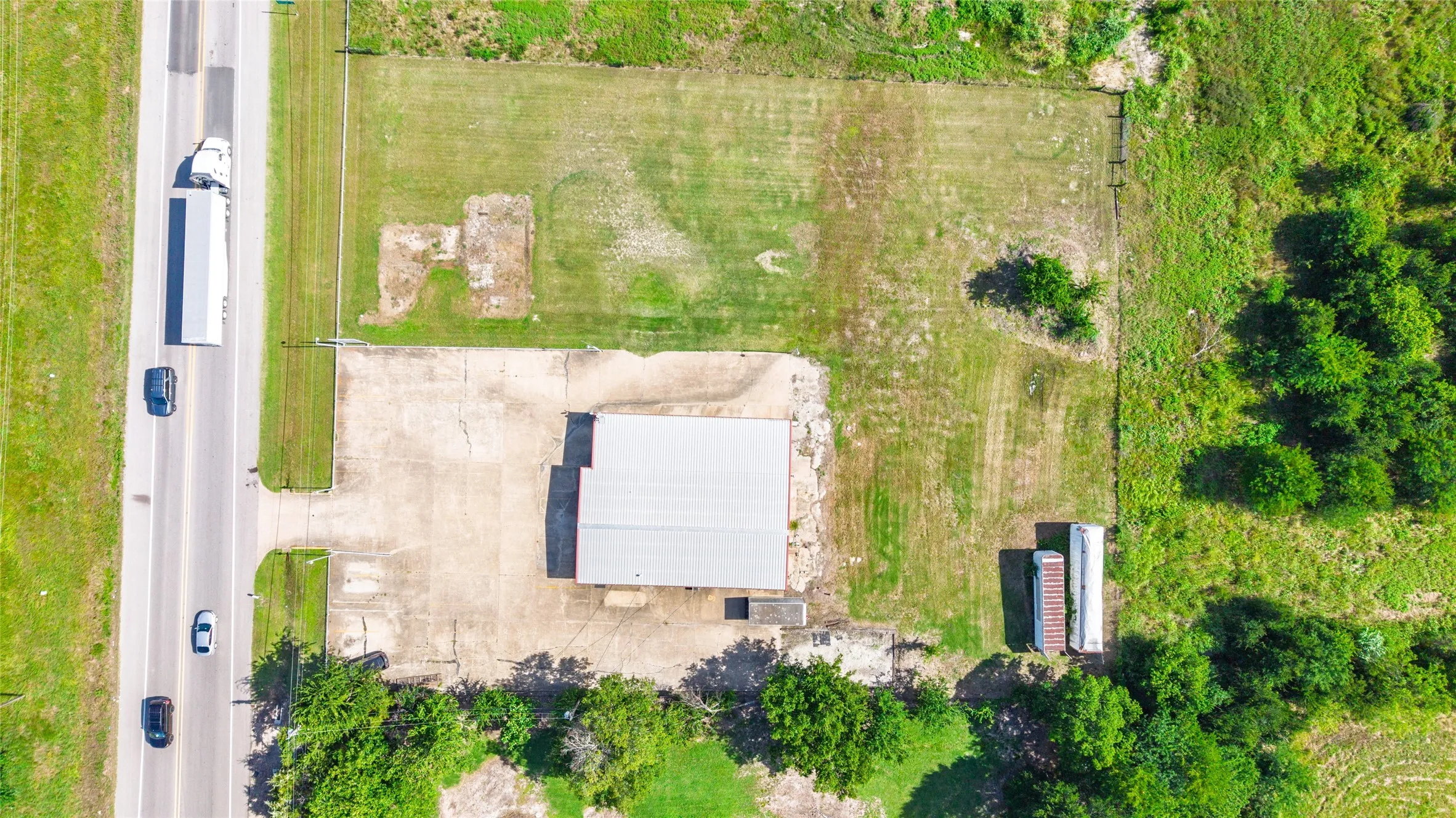 Aerial perspective showcasing a commercial property with a central building featuring a light-colored roof, surrounded by expansive green space