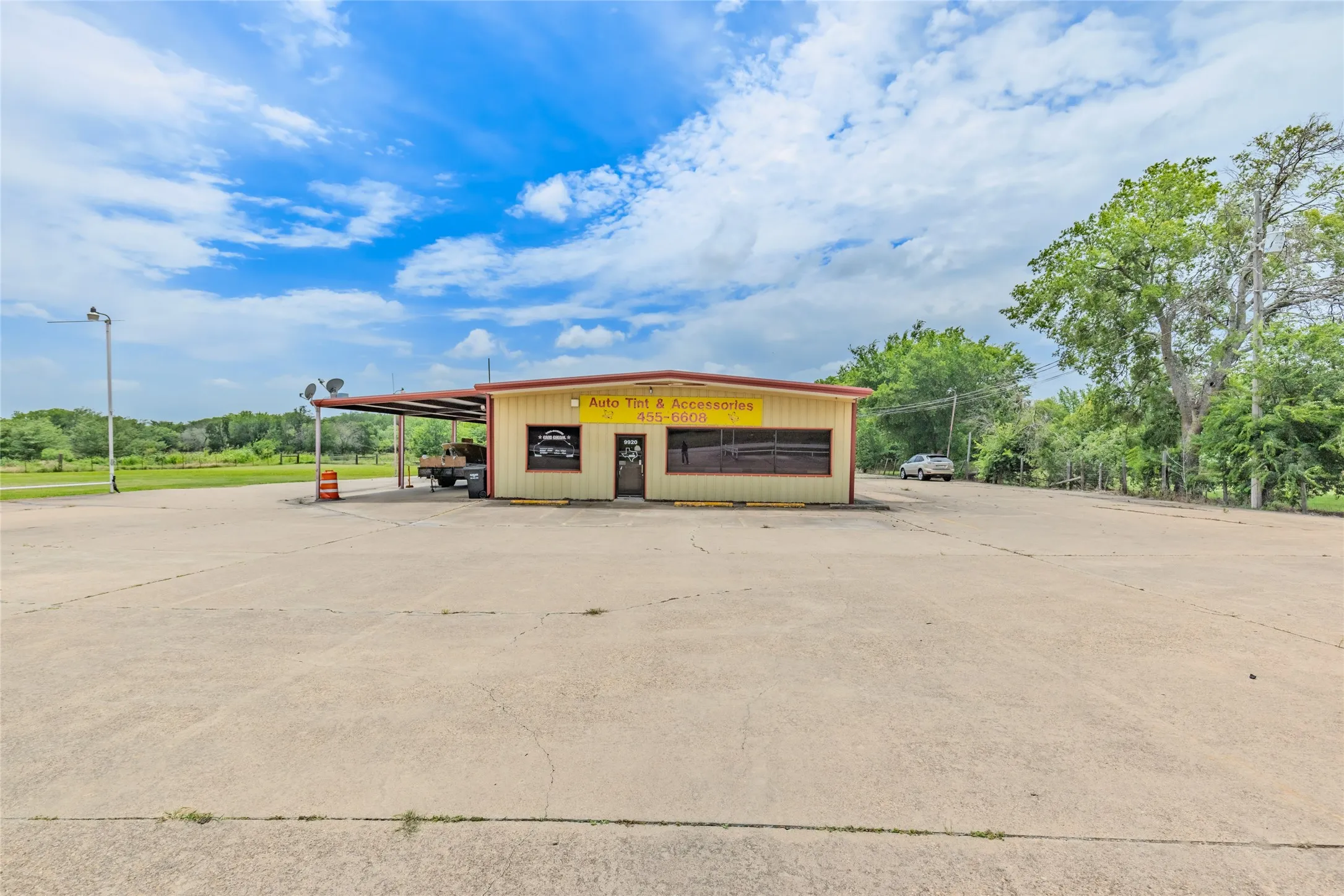 Commercial building featuring a large concrete parking area, a covered carport extension, and a prominent storefront with multiple windows