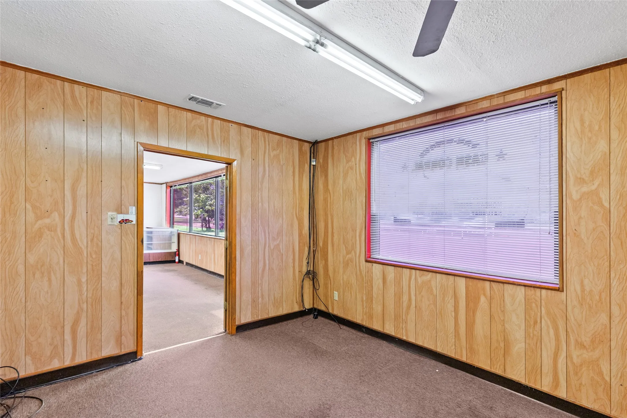 Room featuring wood paneling, carpet flooring, and a drop ceiling with fluorescent lighting