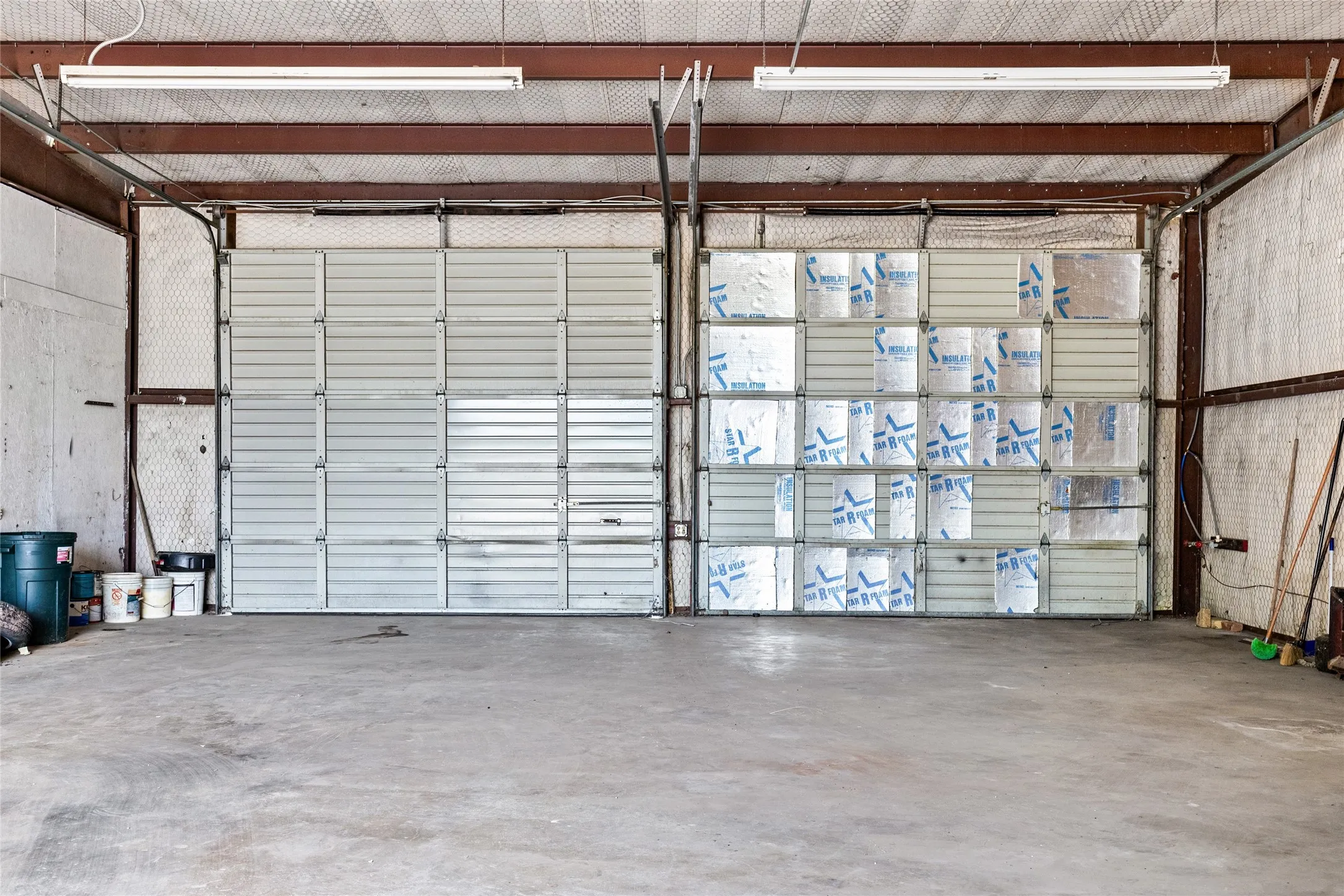 Industrial space featuring a concrete floor, exposed metal beam ceiling, and two overhead garage doors