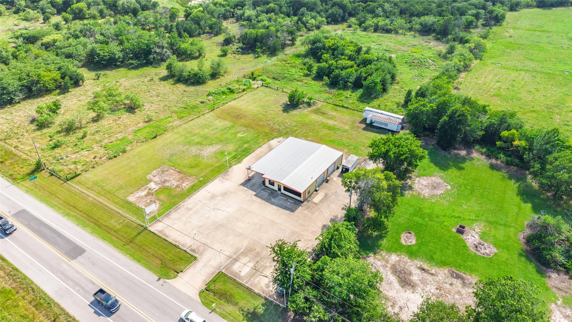 Commercial building with a metal roof and paved parking lot, bordered by a public roadway and expansive green acreage