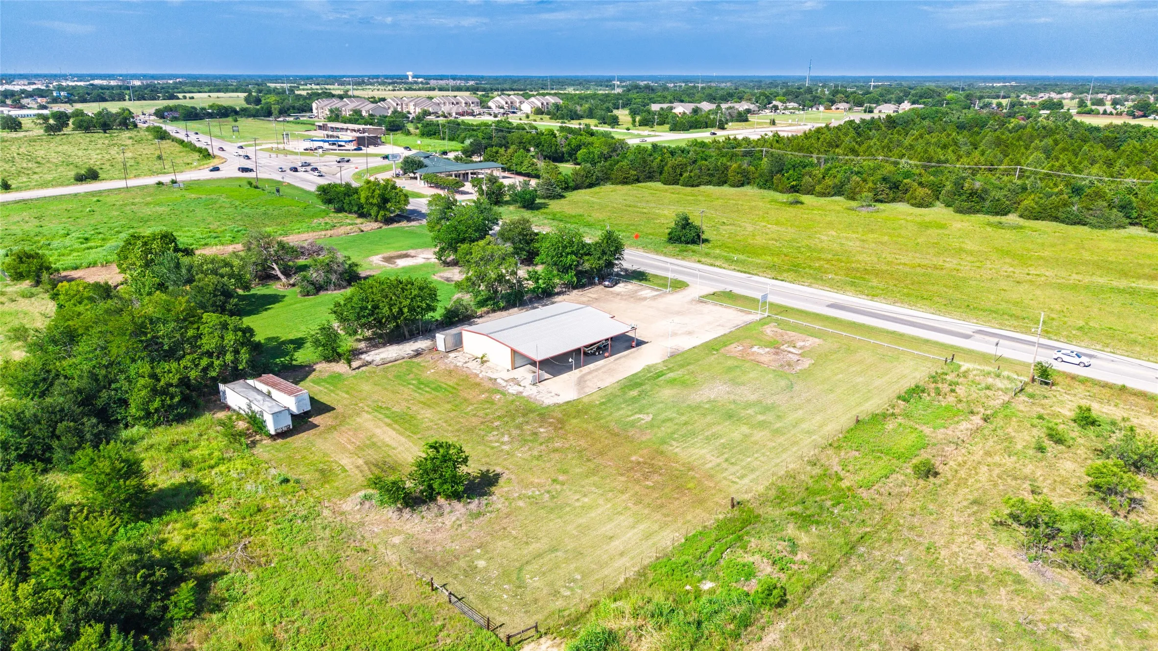Expansive land parcel featuring a metal-roofed structure with an attached covered area, substantial green space, established trees, and direct road frontage