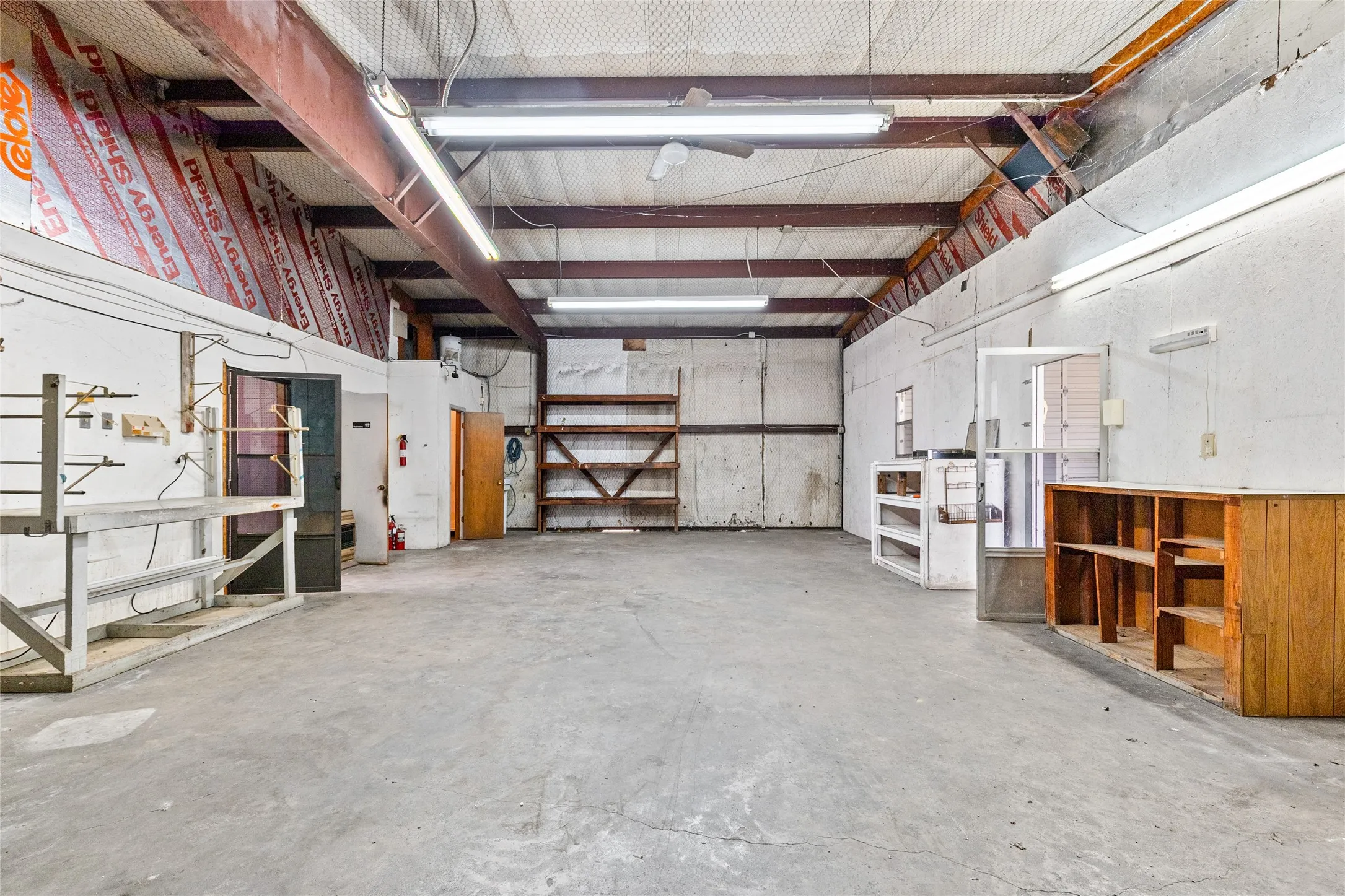 Spacious commercial interior featuring a concrete floor, exposed structural beams, and fluorescent lighting