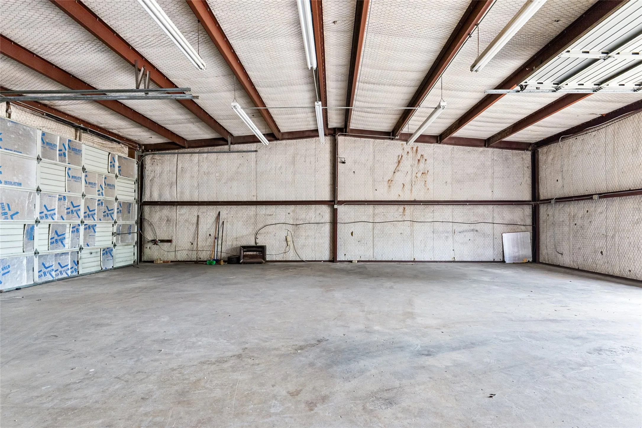 Spacious interior featuring a concrete floor, exposed structural beams, and fluorescent lighting fixtures