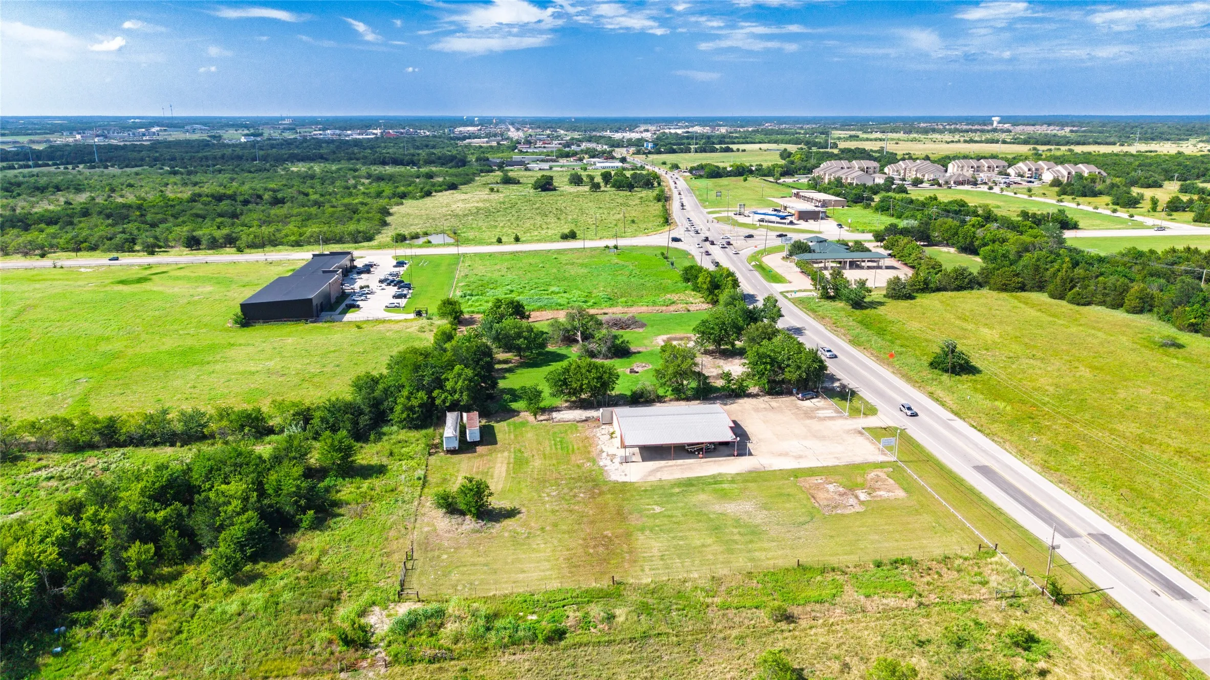 Expansive green acreage featuring a single-story structure with an attached carport, multiple outbuildings, and a tree-lined perimeter