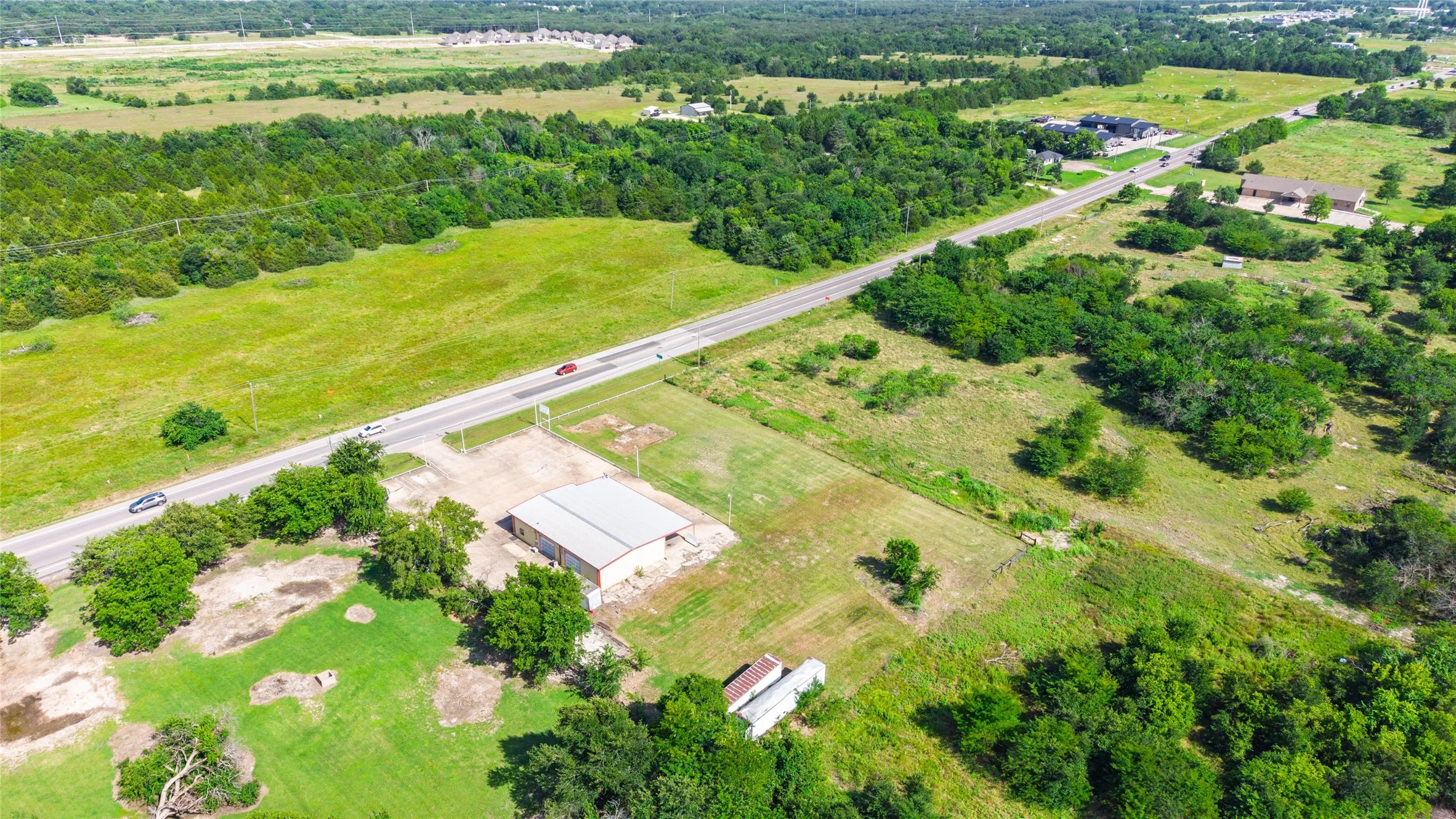 Expansive land parcel featuring a metal-roofed structure, direct road frontage, and a mix of cleared and wooded areas