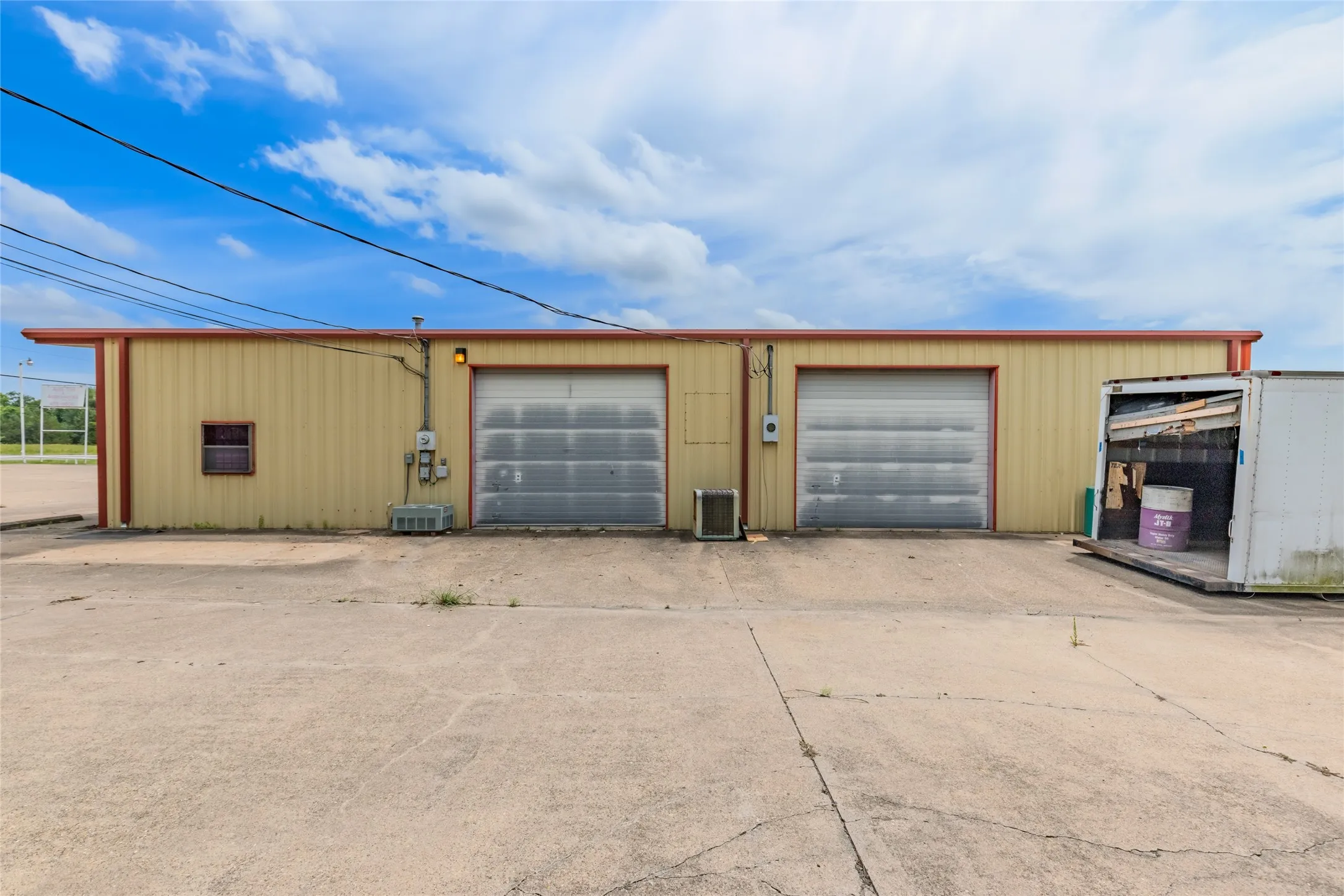 Industrial building featuring a corrugated metal exterior, dual roll-up garage doors, exterior lighting, and a paved lot