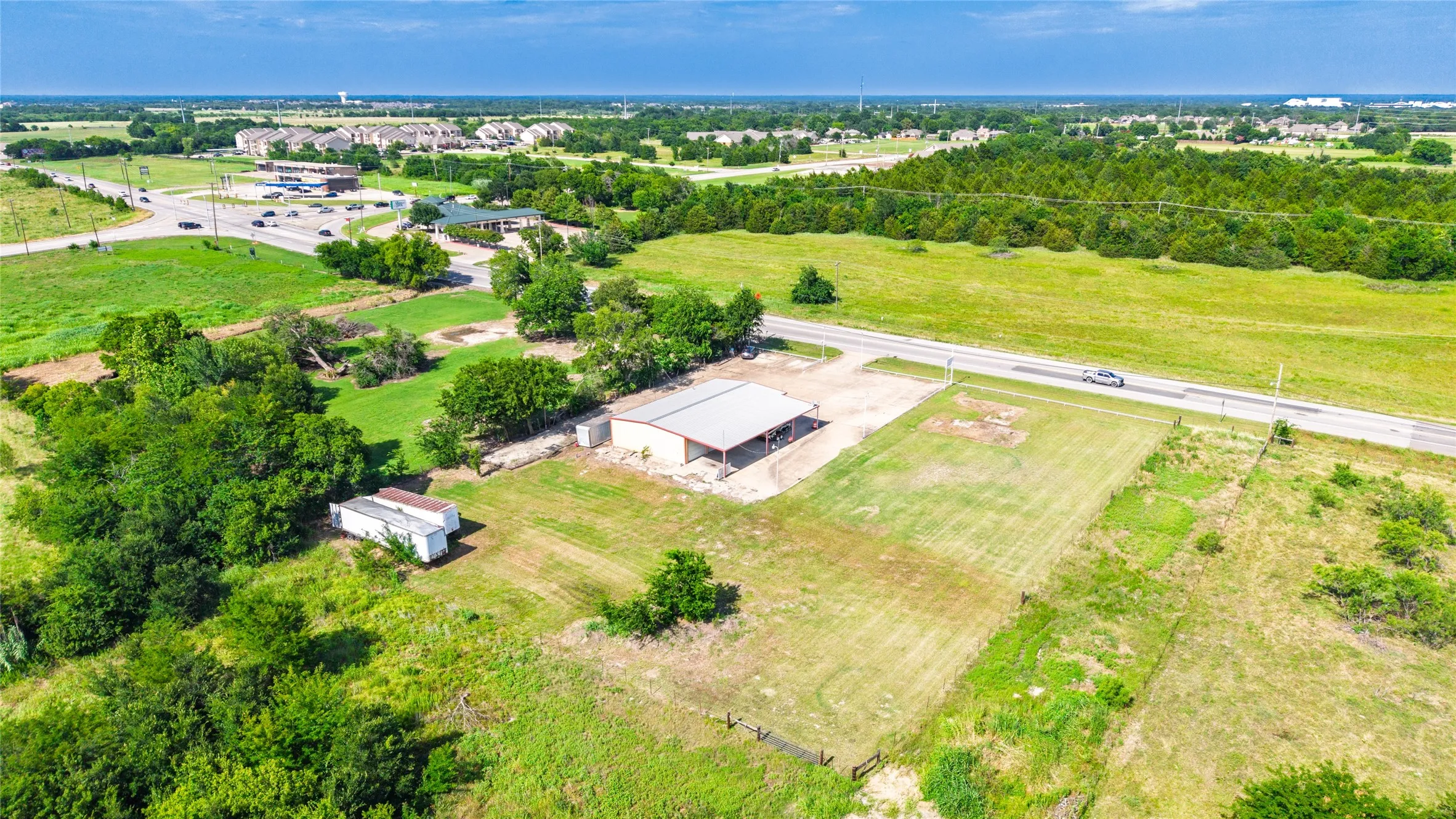 Expansive property featuring a large open-sided building with a metal roof, two white storage structures, a paved drive, and abundant green space