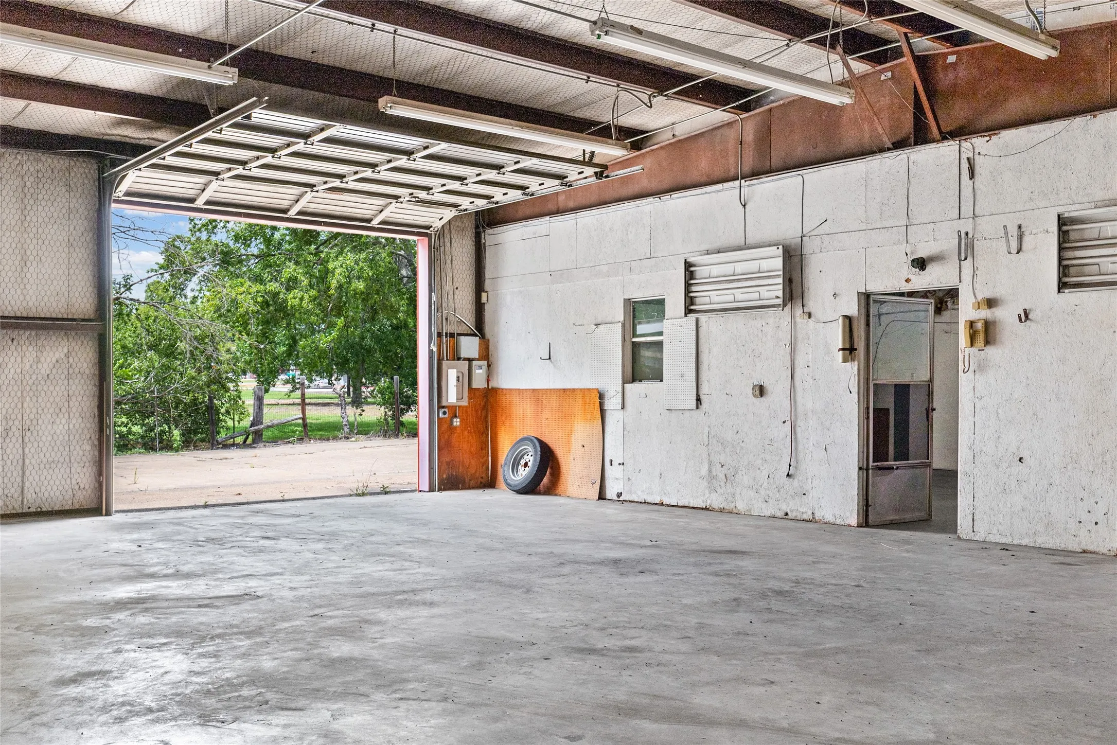 Spacious interior featuring a concrete floor, high ceilings with exposed beams, and fluorescent lighting