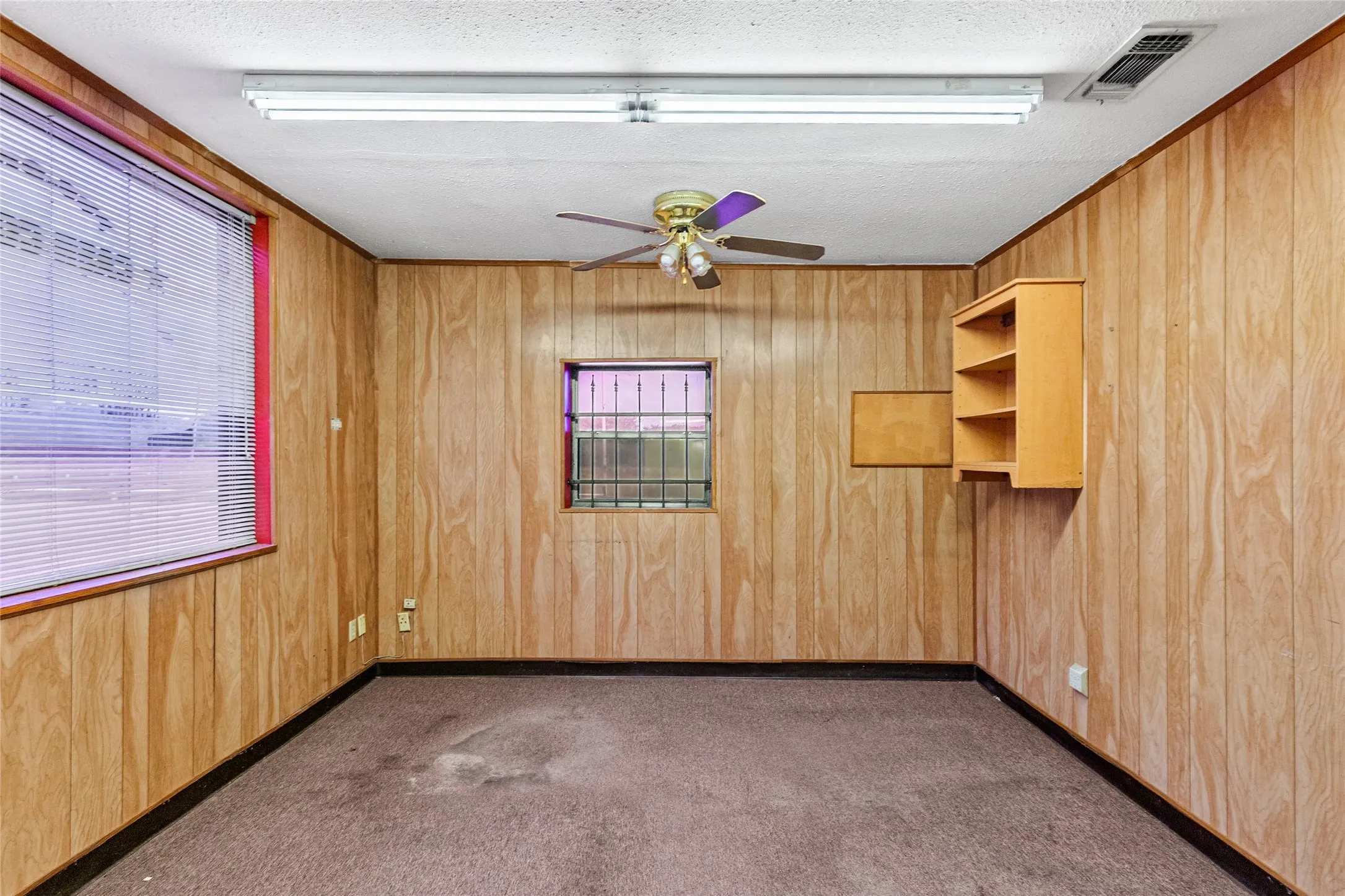 Wood-finish wall paneling throughout, featuring a ceiling fan with light fixture and fluorescent overhead lighting